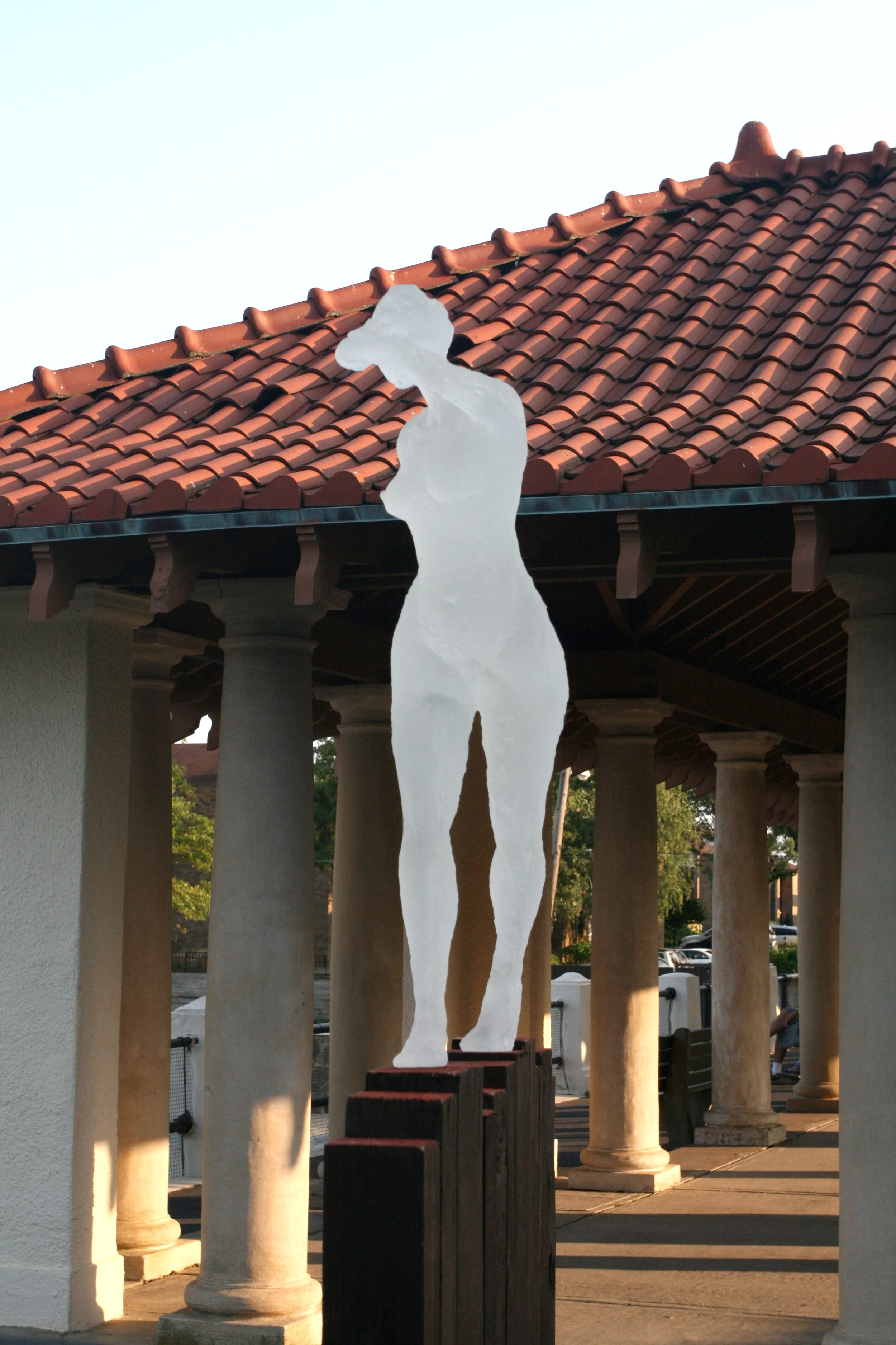 A white silhouette of a female figure sculpture positioned between columns with a tiled rooftop and trees in the background.