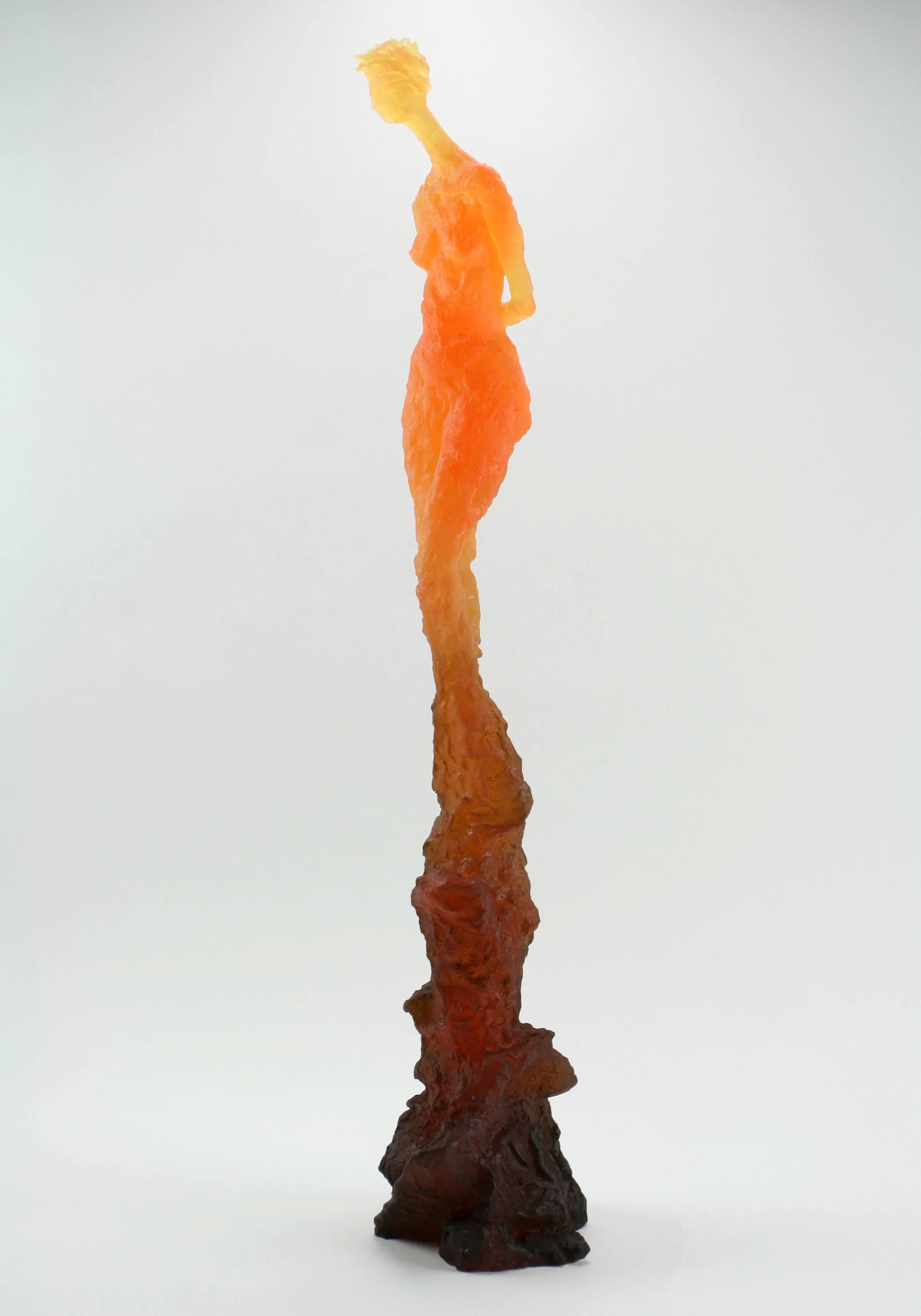 Colorful, elongated sculpture resembling a stylized human figure with a yellow head, orange torso, and dark brown base, standing against a plain white background.