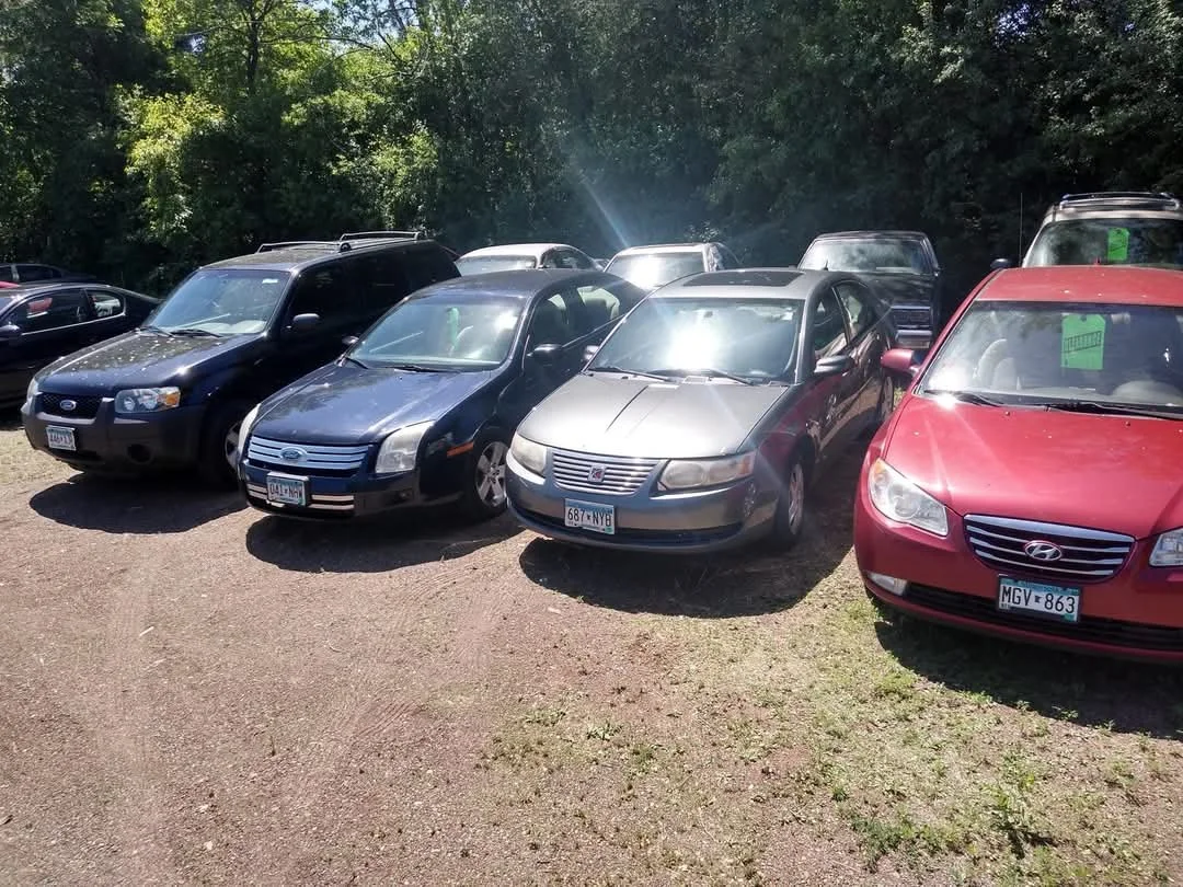 A parking lot with several reasonable priced vehicles including a black SUV, a black sedan, a silver sedan, a red sedan, and in good condition trucks