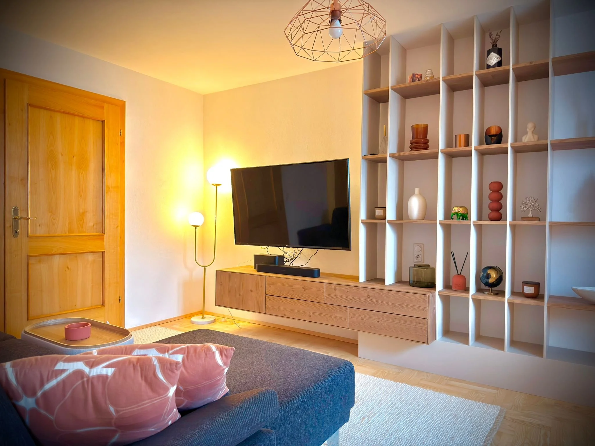 Modernes Wohnzimmer mit Holzdekor, Fernseher, Stehlampe, offene Regal mit Dekorationsgegenständen und Rattansesseln.