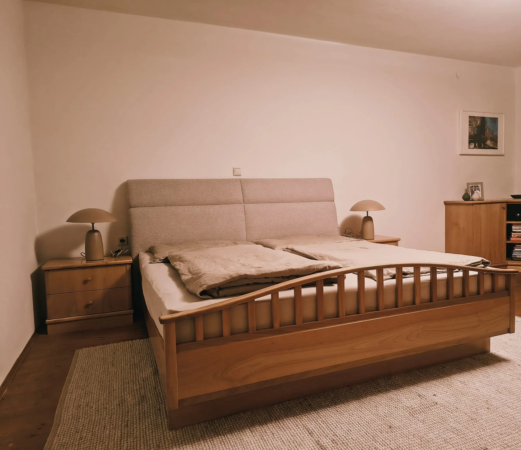 Schlafzimmer mit Holzbett, zwei Nachttischen mit Lampen, einem Schrank und Wanddekorationen.