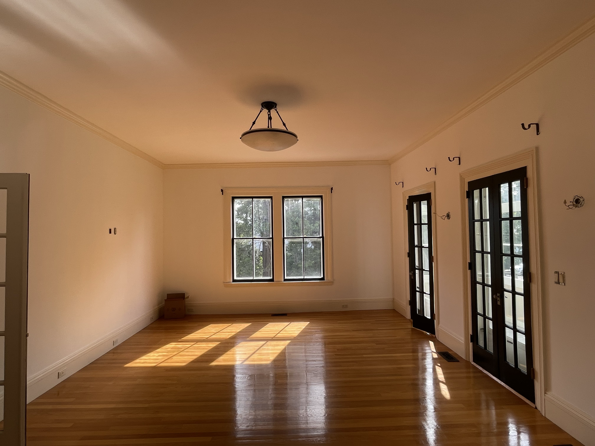 Empty room with window and glass door, hardwood floors, and beige walls illuminated by sunlight.