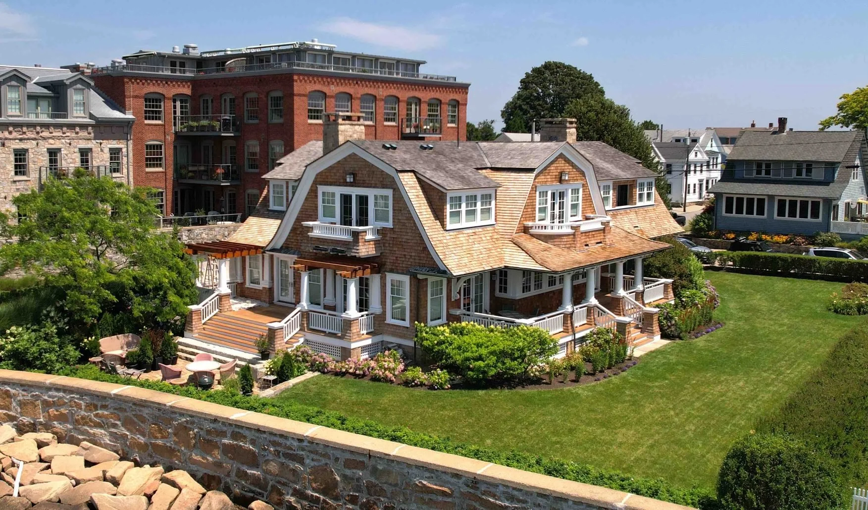 Photo of a large traditional house with a landscaped yard, shrubs, and flowers, surrounded by other residential buildings.
