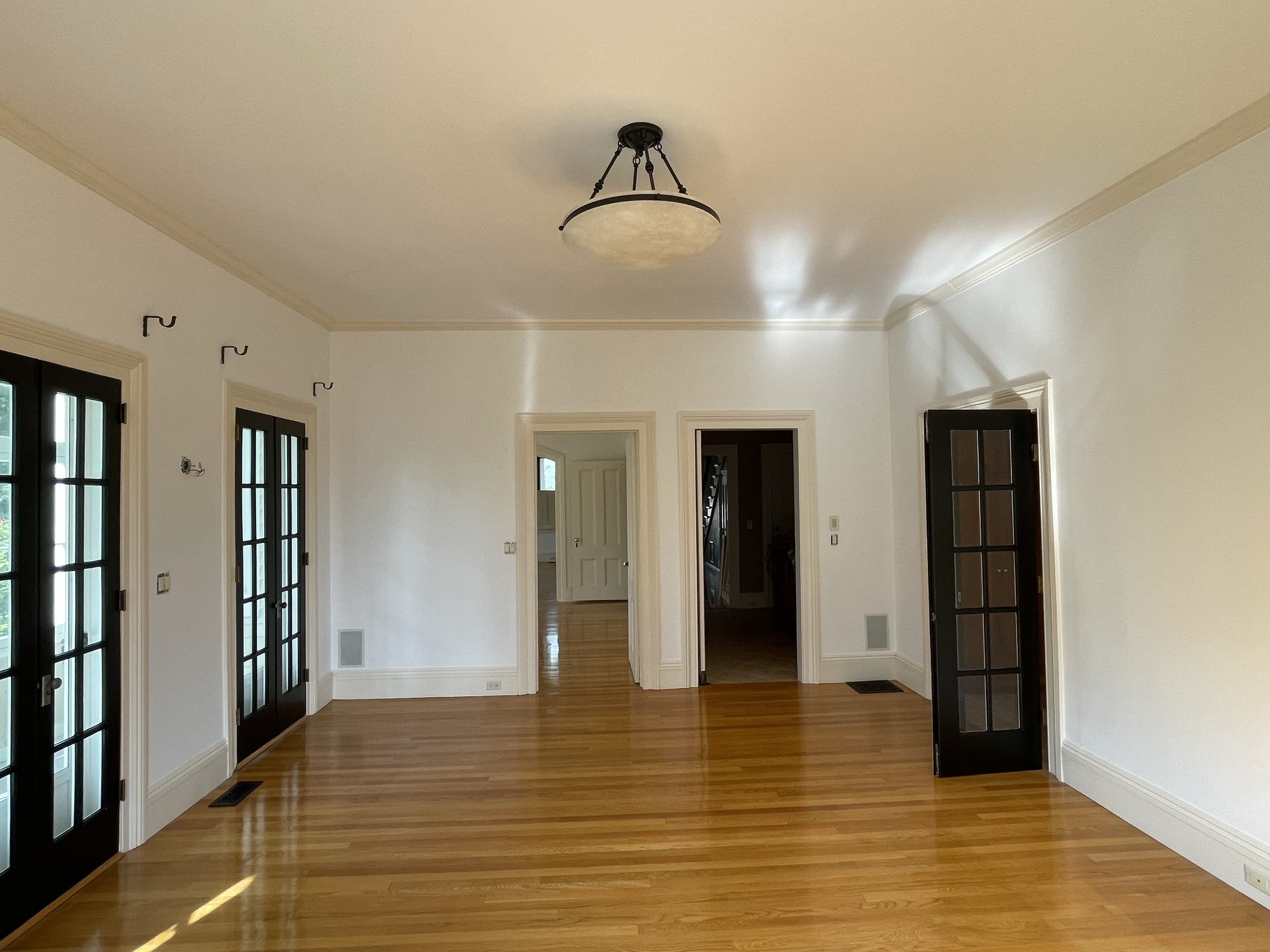 Empty living room with hardwood floors, white walls, and black French doors, with a ceiling light fixture.