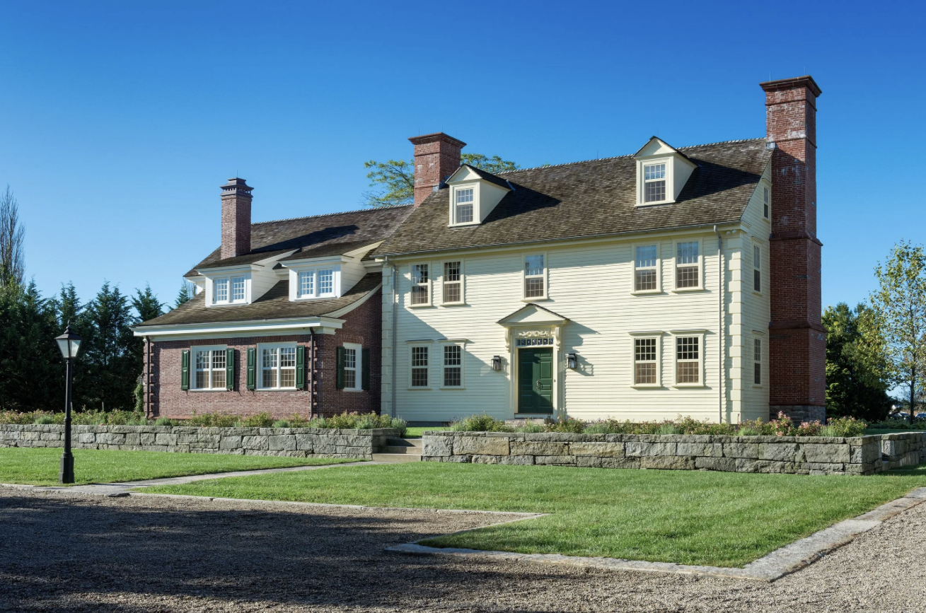 A large, historic house with a mix of brick and white siding exterior, multiple chimneys, and dormer windows on a well-maintained lawn.