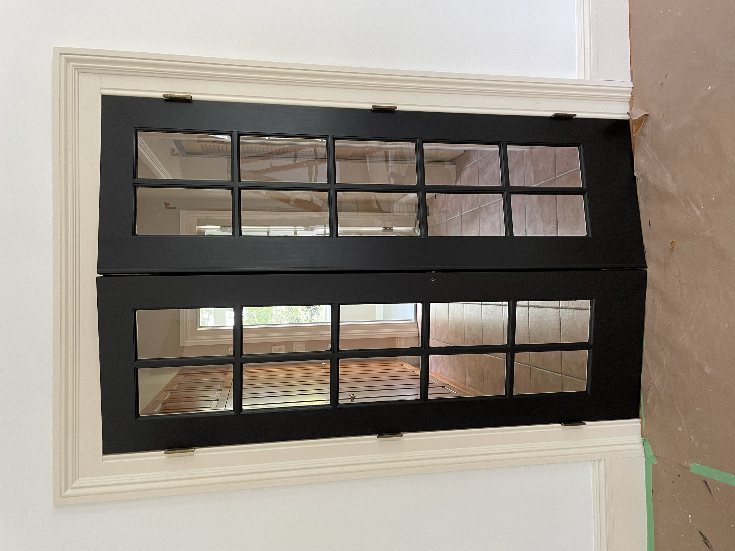 A black framed glass door leading into a room with tiled flooring and wooden cabinetry, seen through the glass panels.