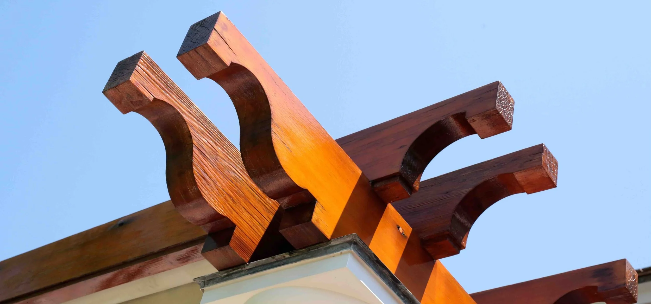 Close-up of a wooden architectural detail with curved beams against a clear blue sky.