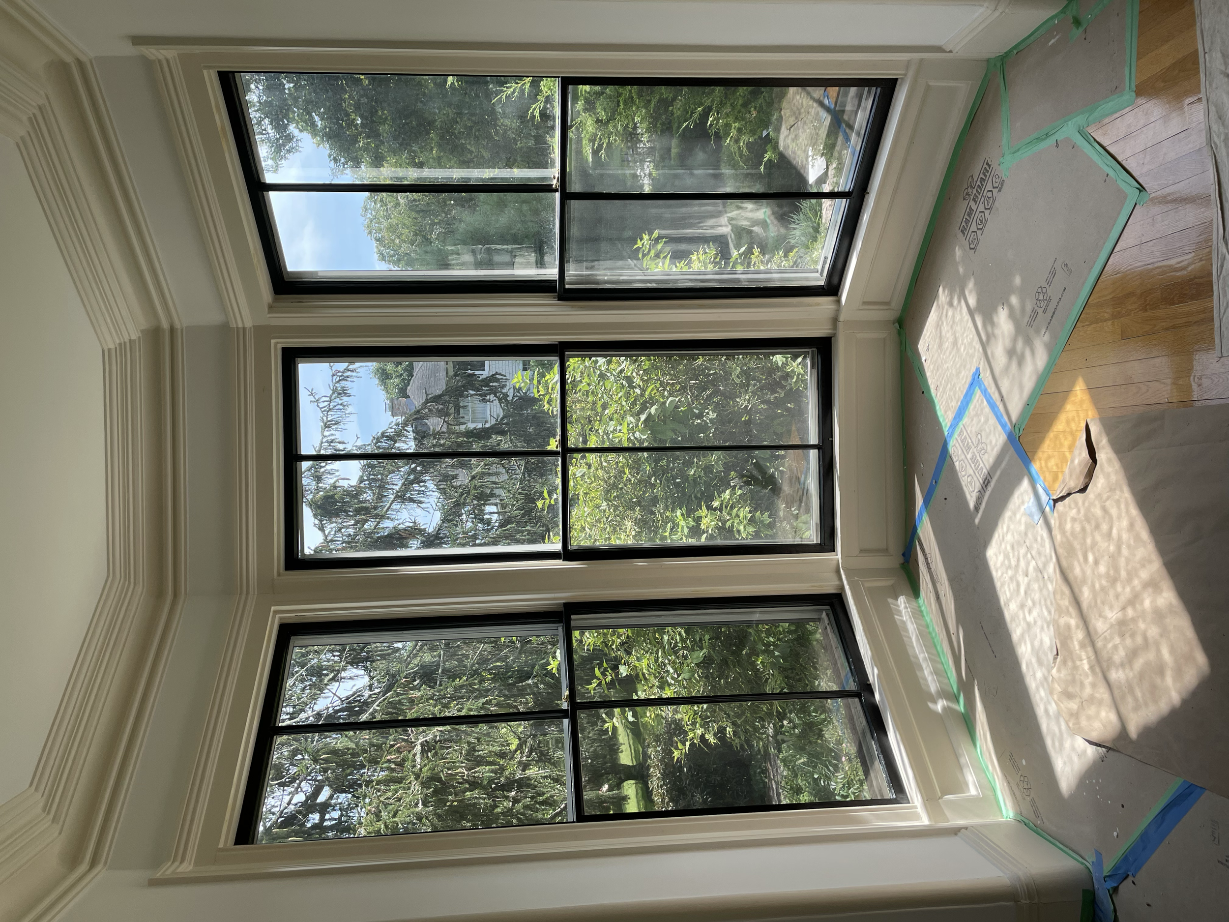 Interior room with large window, white walls, and a cardboard box on the floor, taped with green painter's tape.