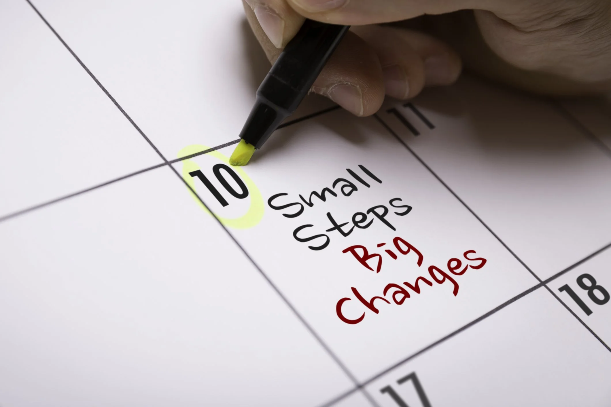 A hand highlighting the number 10 on a calendar with a yellow marker, with handwritten note saying 'Small Steps' in black and 'Big Changes' in red.