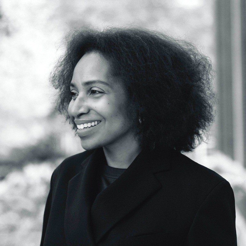 Black and white portrait of a smiling woman with natural, voluminous curly hair, wearing a dark blazer.