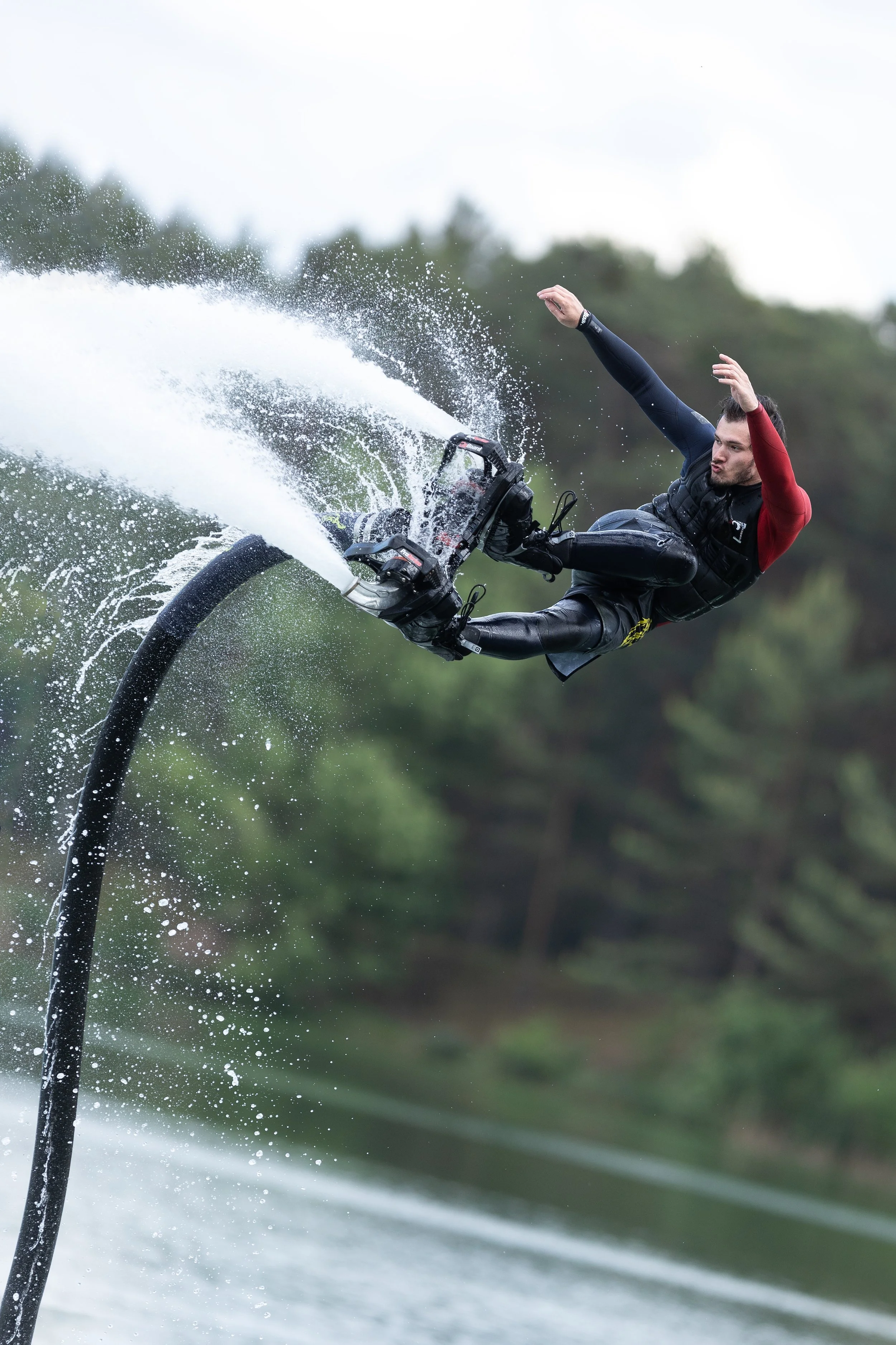 Muž v neoprenu předvádí trik na vodním jetboardu na řece, zaklání se dozadu, zatímco za ním stříká voda.