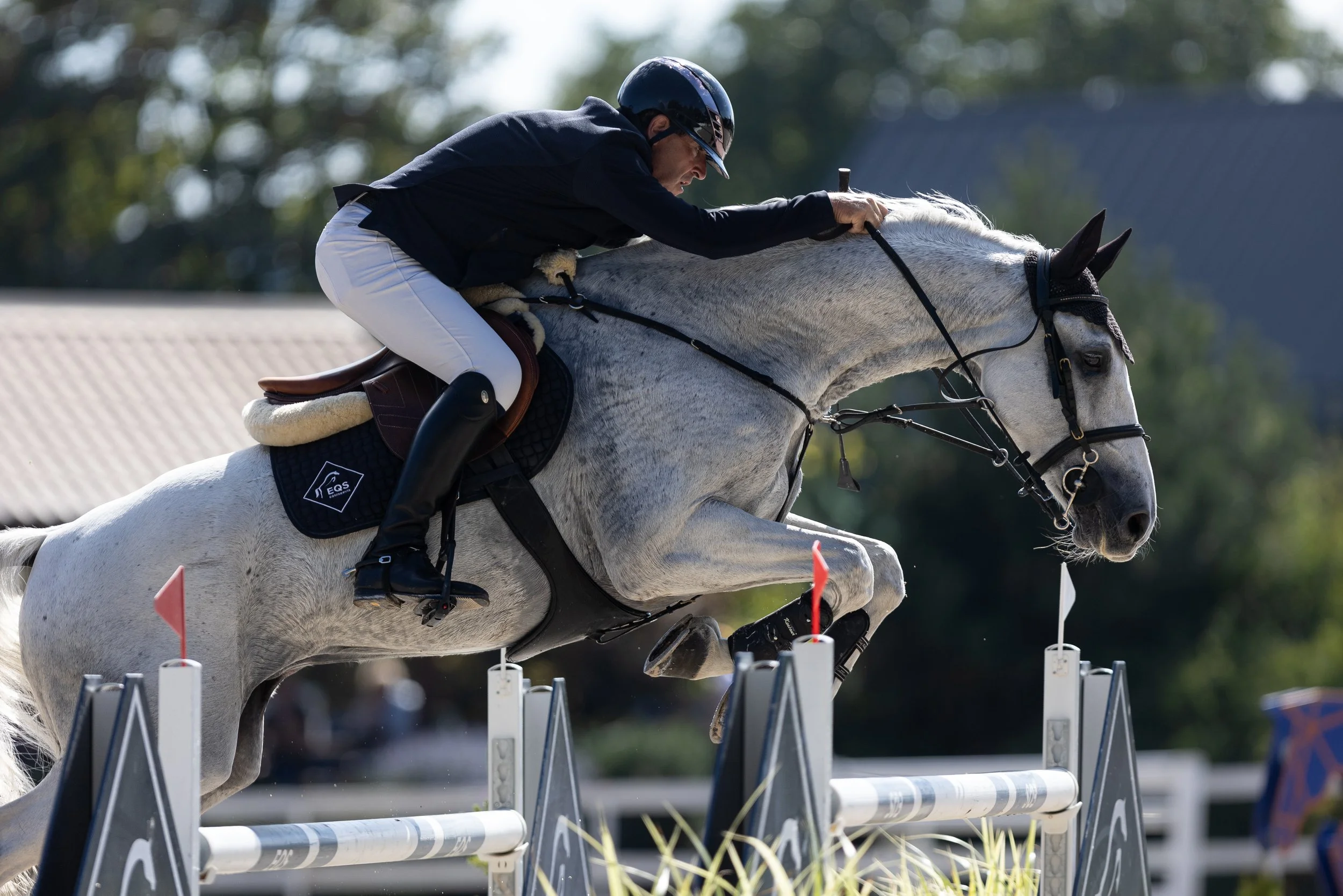 Osoba na šedém koni skáče přes překážku během venkovní parkurové soutěže.
