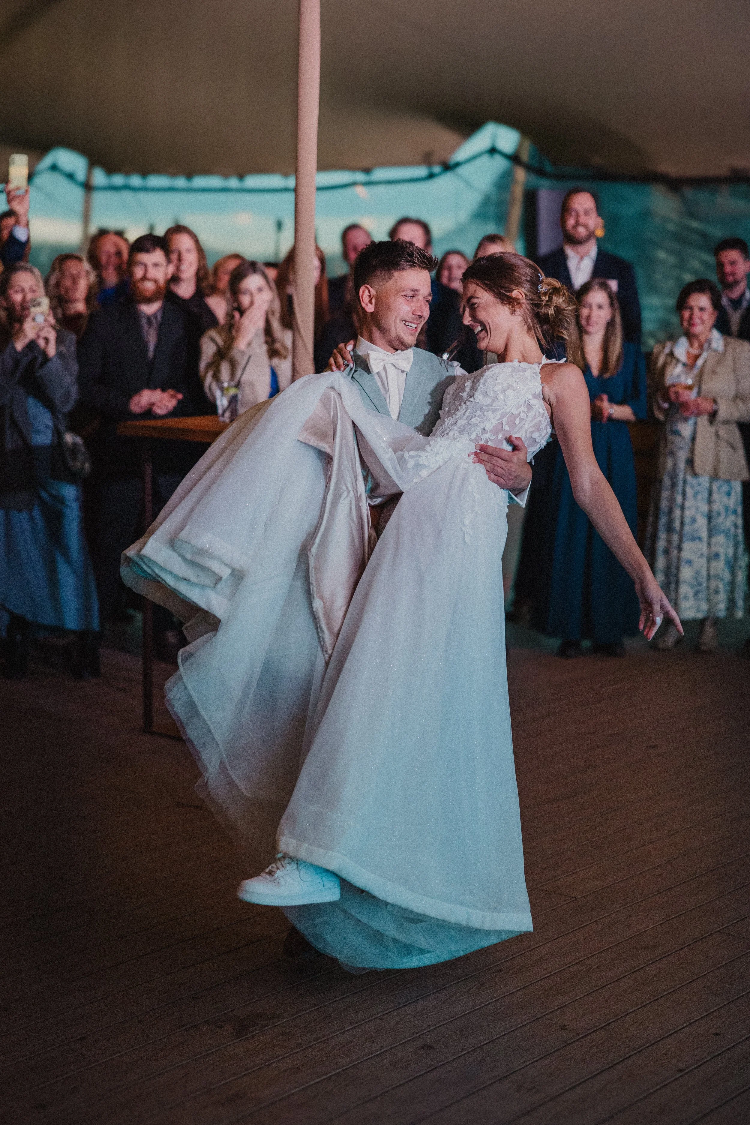 Nevěsta a ženich tančí na svatební hostině, zatímco hosté v pozadí sledují a fotí.