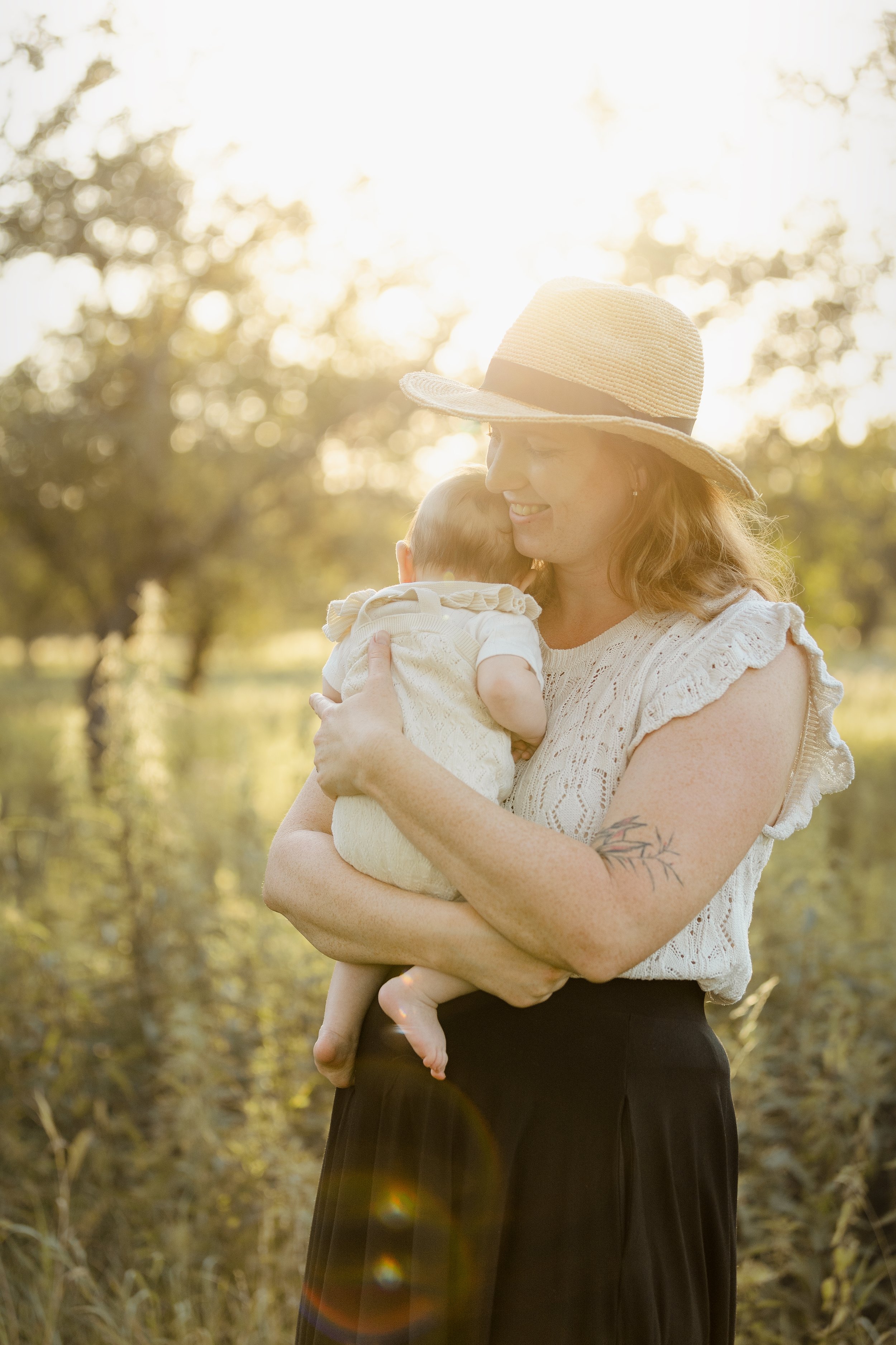 Žena v klobouku drží malé dítě venku při západu slunce.