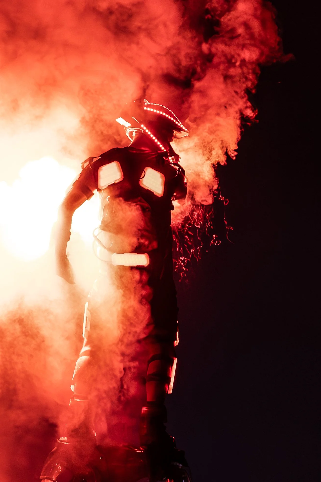 Osoba jede na flyboardu v noci, s barevnými světly a kouřem v pozadí.