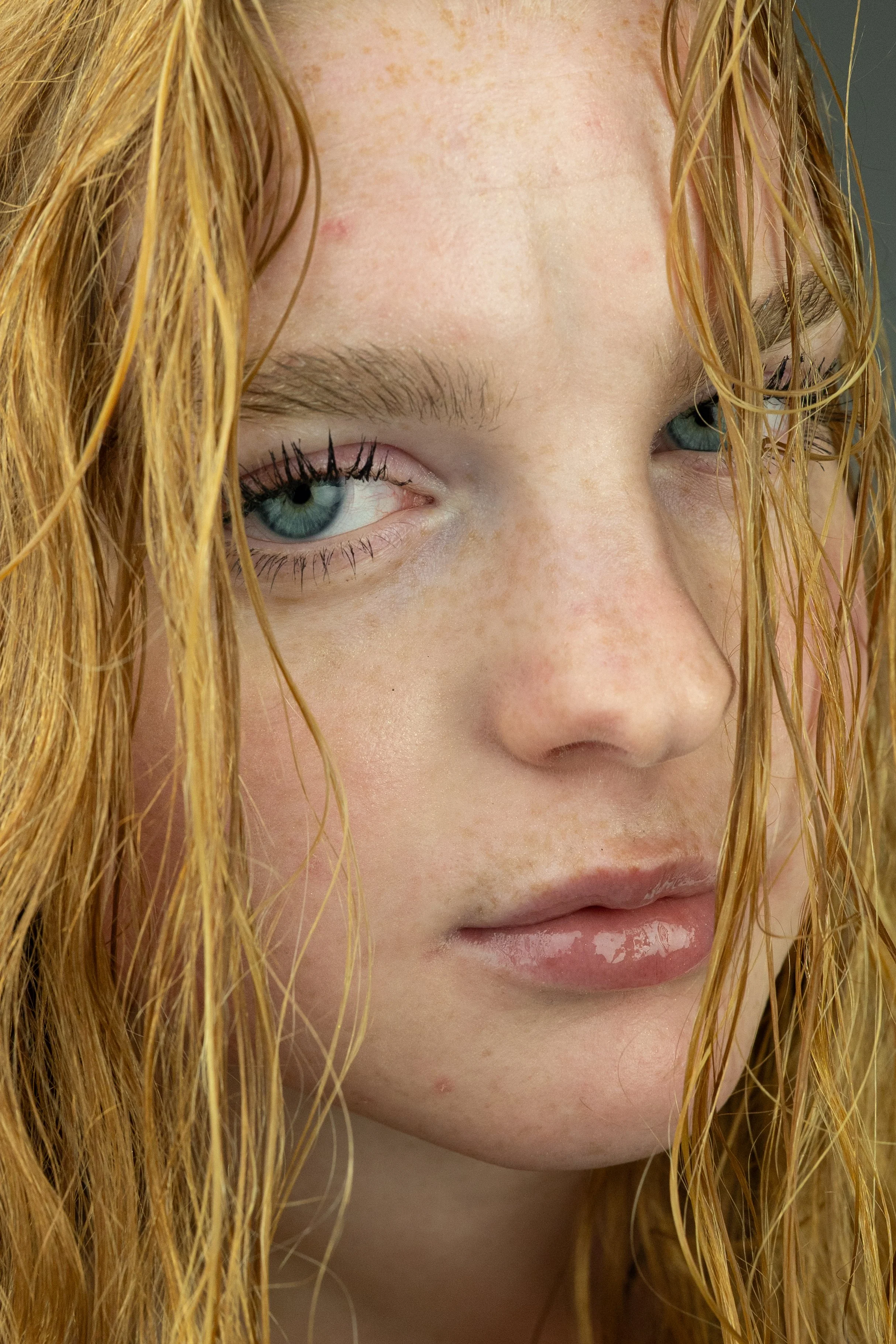 Detailní záběr mladé ženy s mokrými zrzavými vlasy a modrýma očima, dívající se lehce stranou.