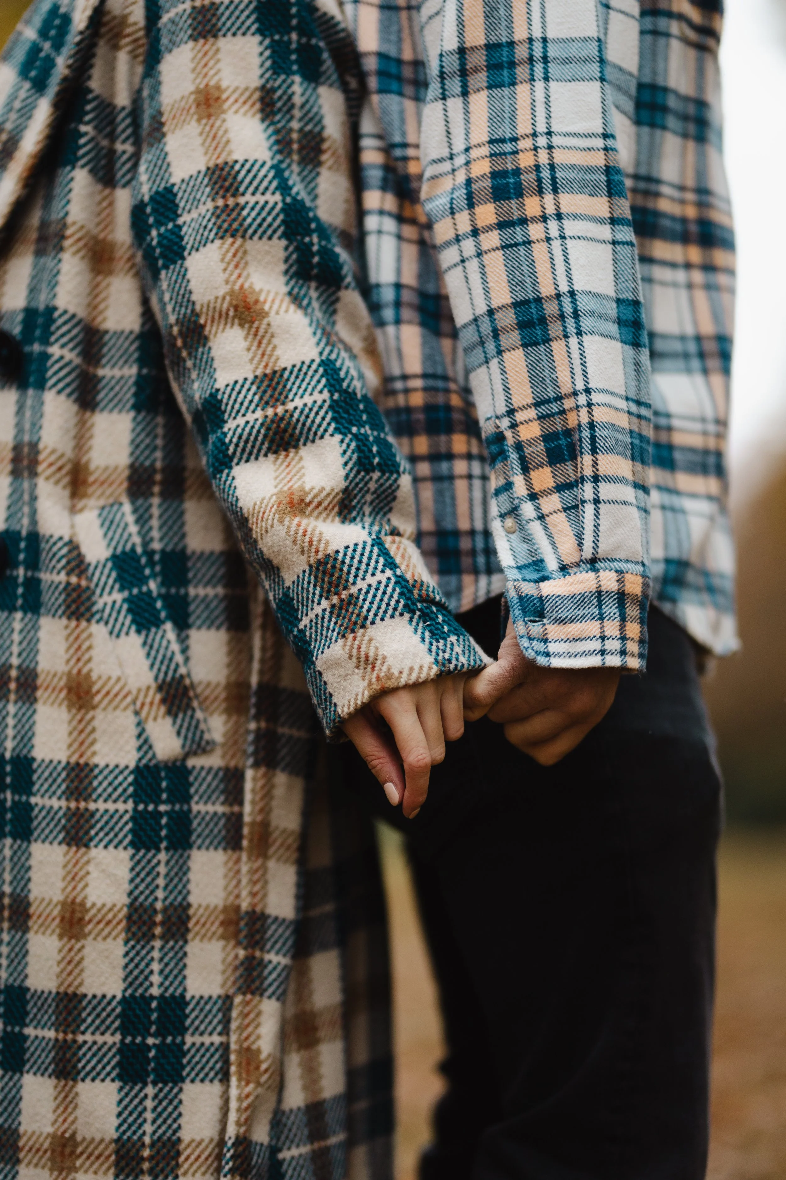 Detail dvou lidí držících se za ruce, v kostkovaných košilích, venku.