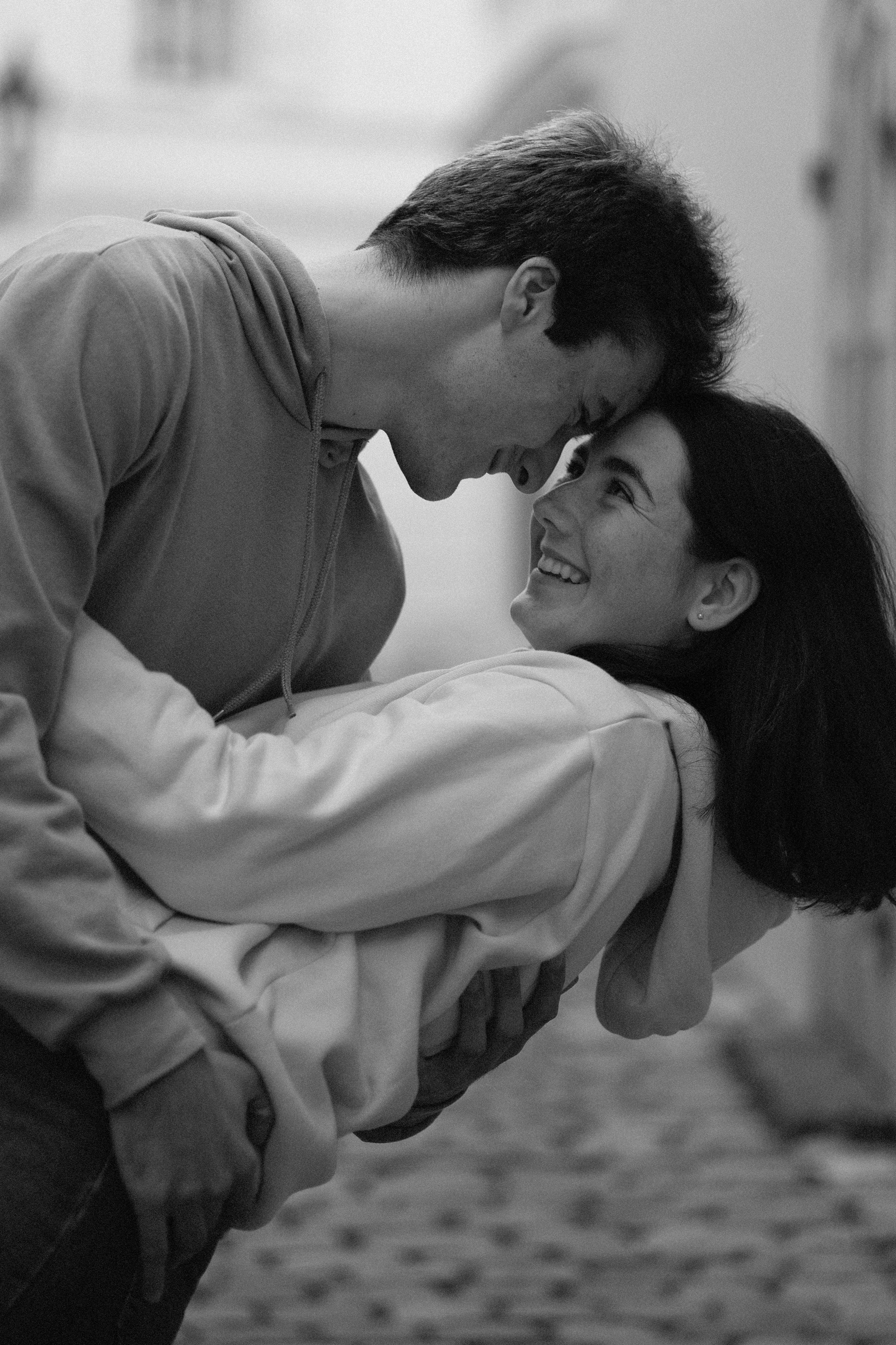 Černobílá fotografie mladého muže a ženy, kteří se usmívají a jsou těsně u sebe; muž se naklání nad ženu, která se na něj usmívá.