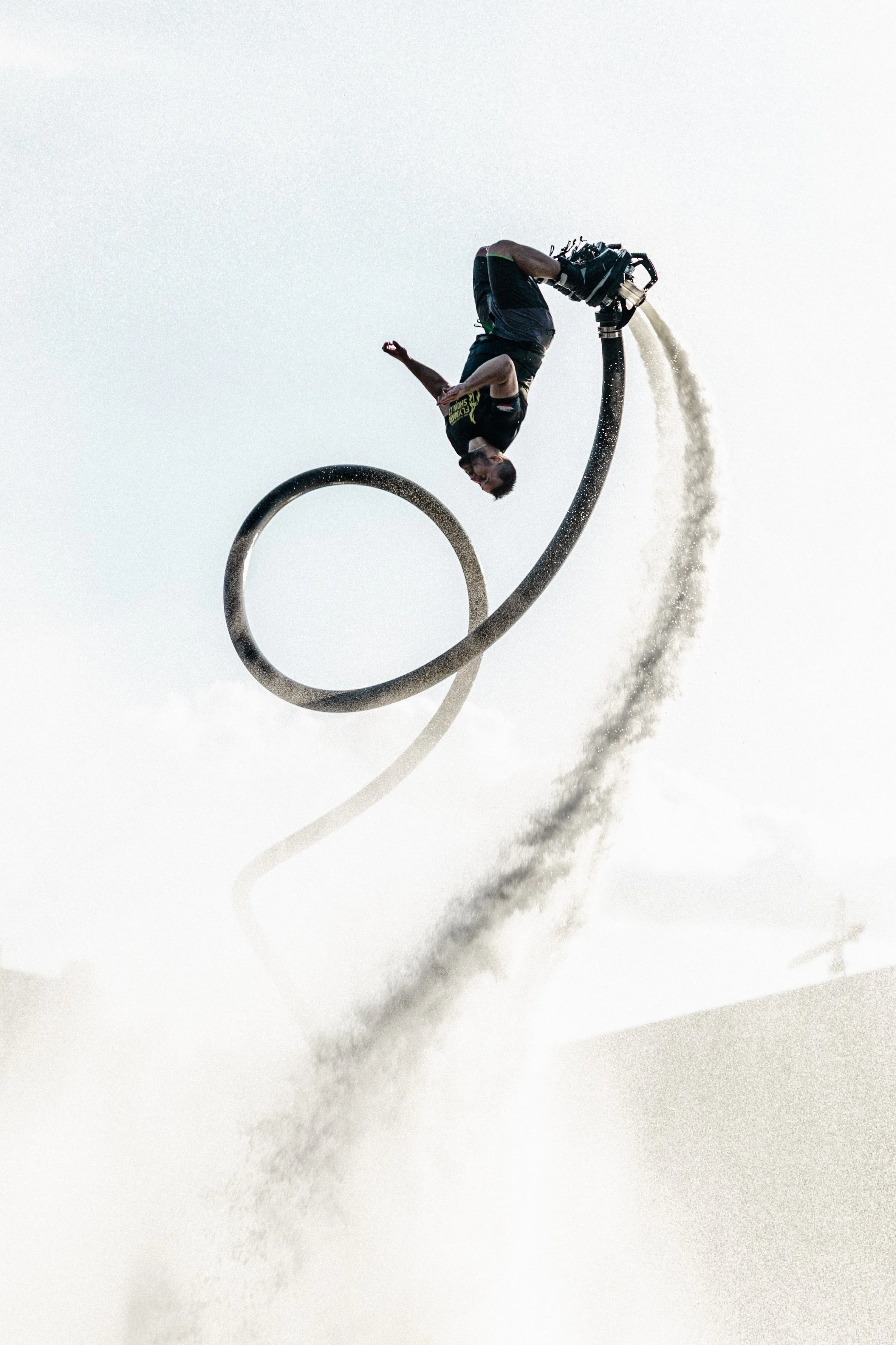 Osoba předvádí trik na velké smyčkové vodní skluzavce, ve vzduchu, zatímco z trysky na konci skluzavky stříká voda.
