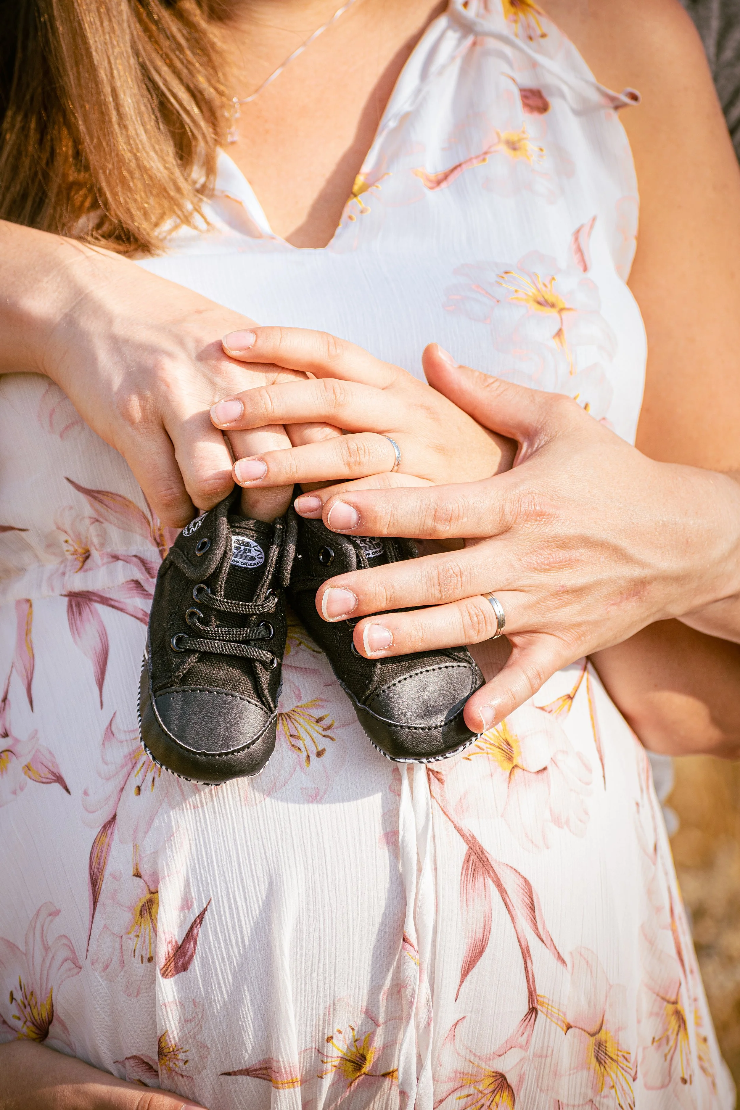 Žena drží pár malých černých dětských botiček na svém těhotenském bříšku.