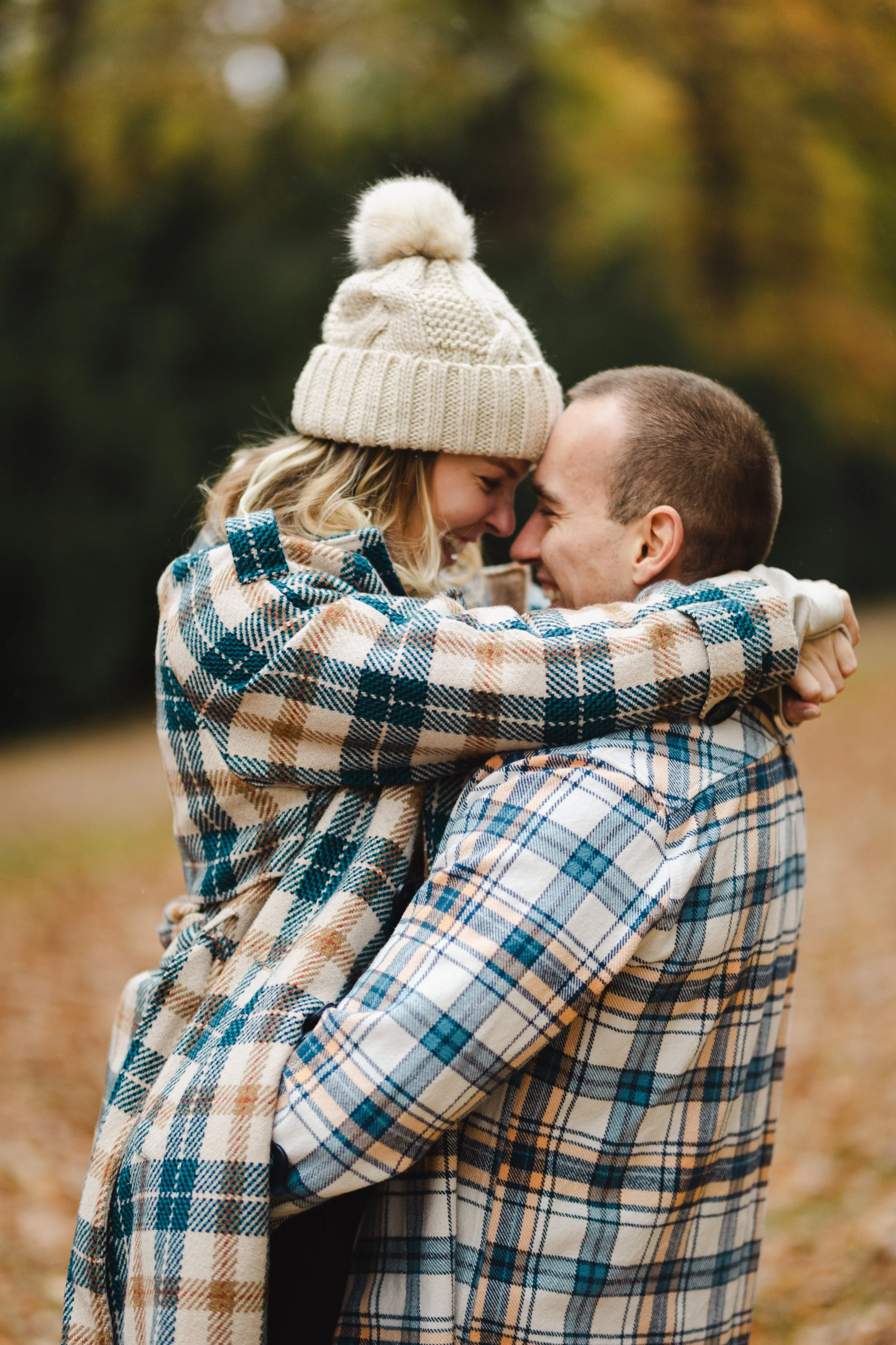 Pár venku během podzimu, těsně se objímající s čely u sebe, oblečený v kostkovaném a pleteném zimním oblečení.