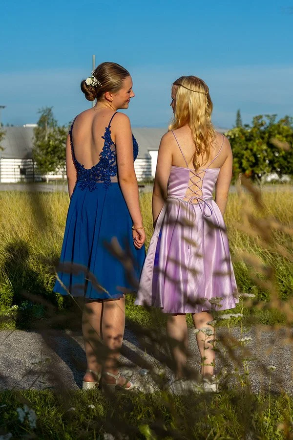 Kaksi nuorta naista puhuu ja hymyilee toisilleen ulkona, pelloilla, kesäpäivänä, todennäköisesti juhliessaan tai kesän yllätysjuhlissa.