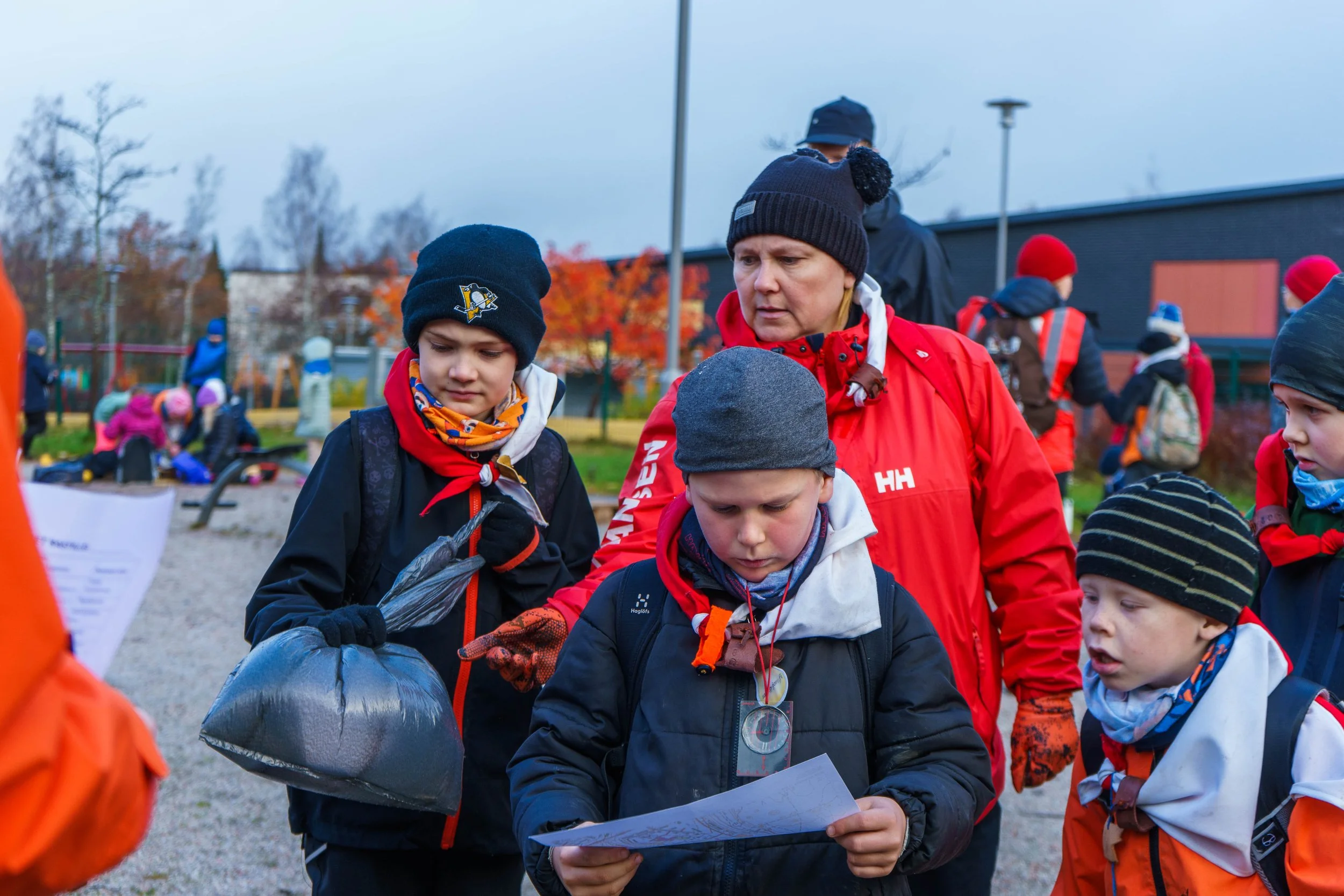 Ryhmä lasten ja ohjaajan ulkona osallistumassa nuotitus- tai reittiharjoitukseen, pukeutuneina talvivaatteisiin.