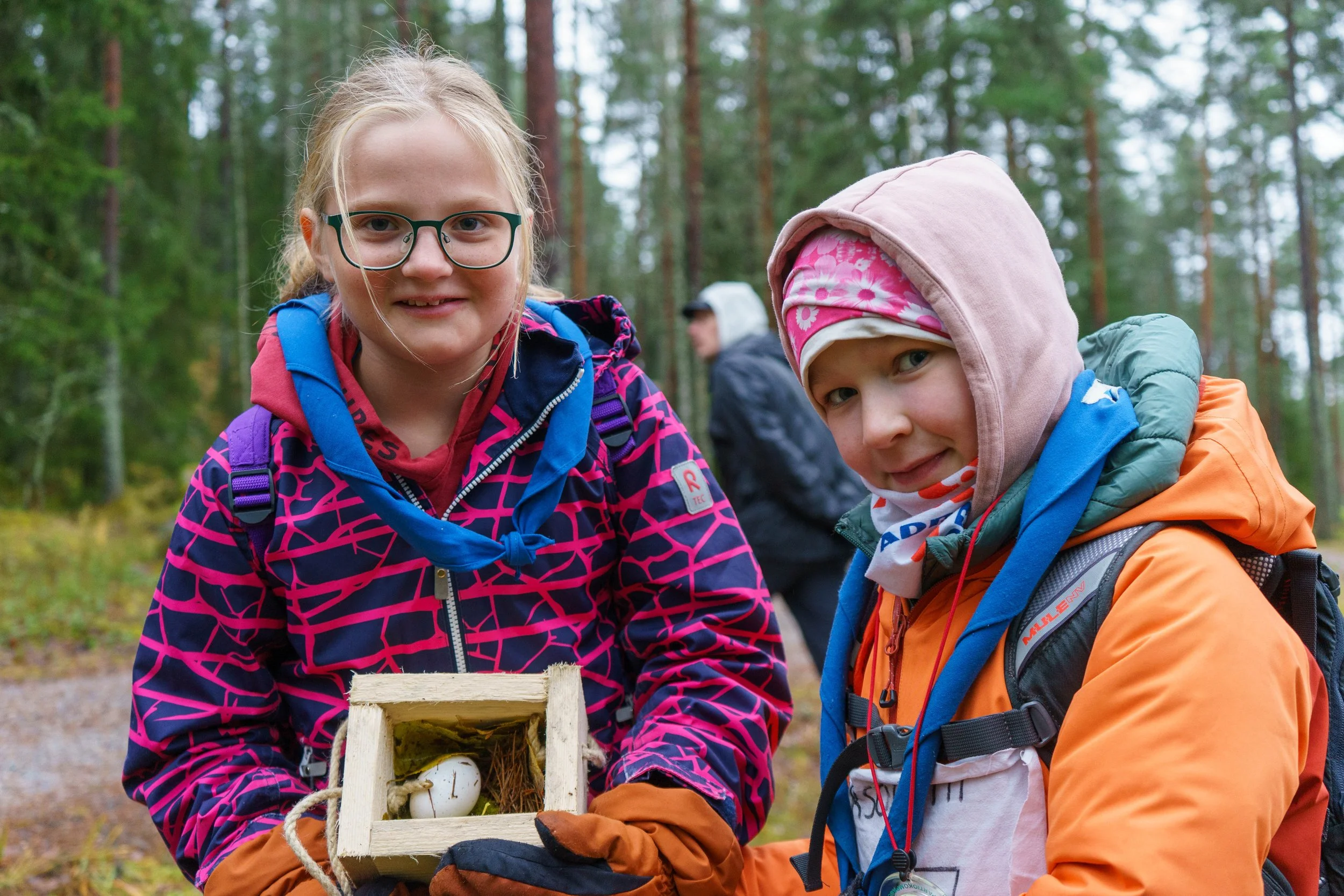 Kaksi lasta metsässä, toinen pitää pientä linnunpönttöä.