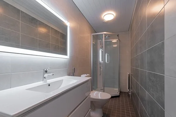 Moderni kylpyhuone, jossa valkoinen allaskaappi, pesuallas, peili ja suihkukaappi.