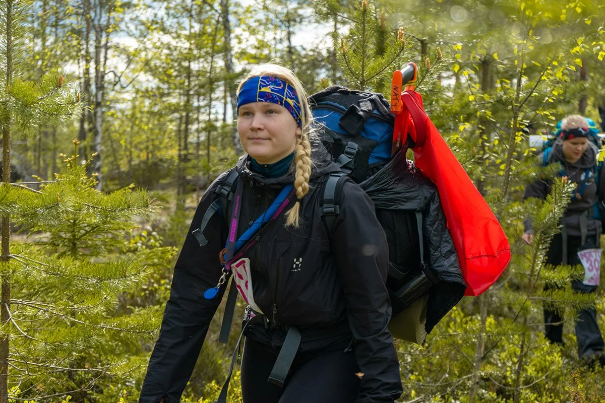 Nuori nainen kantaa suurta reppua kävellessään luonnossa, ympärillään puita ja vihreää kasvillisuutta.