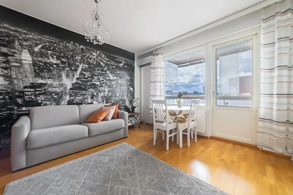 Olohuone, jossa harmaa sohva, neljä valkoista tuolia ja suuri ikkuna näkymällä kaupungin siluettiin ja taivaalle.