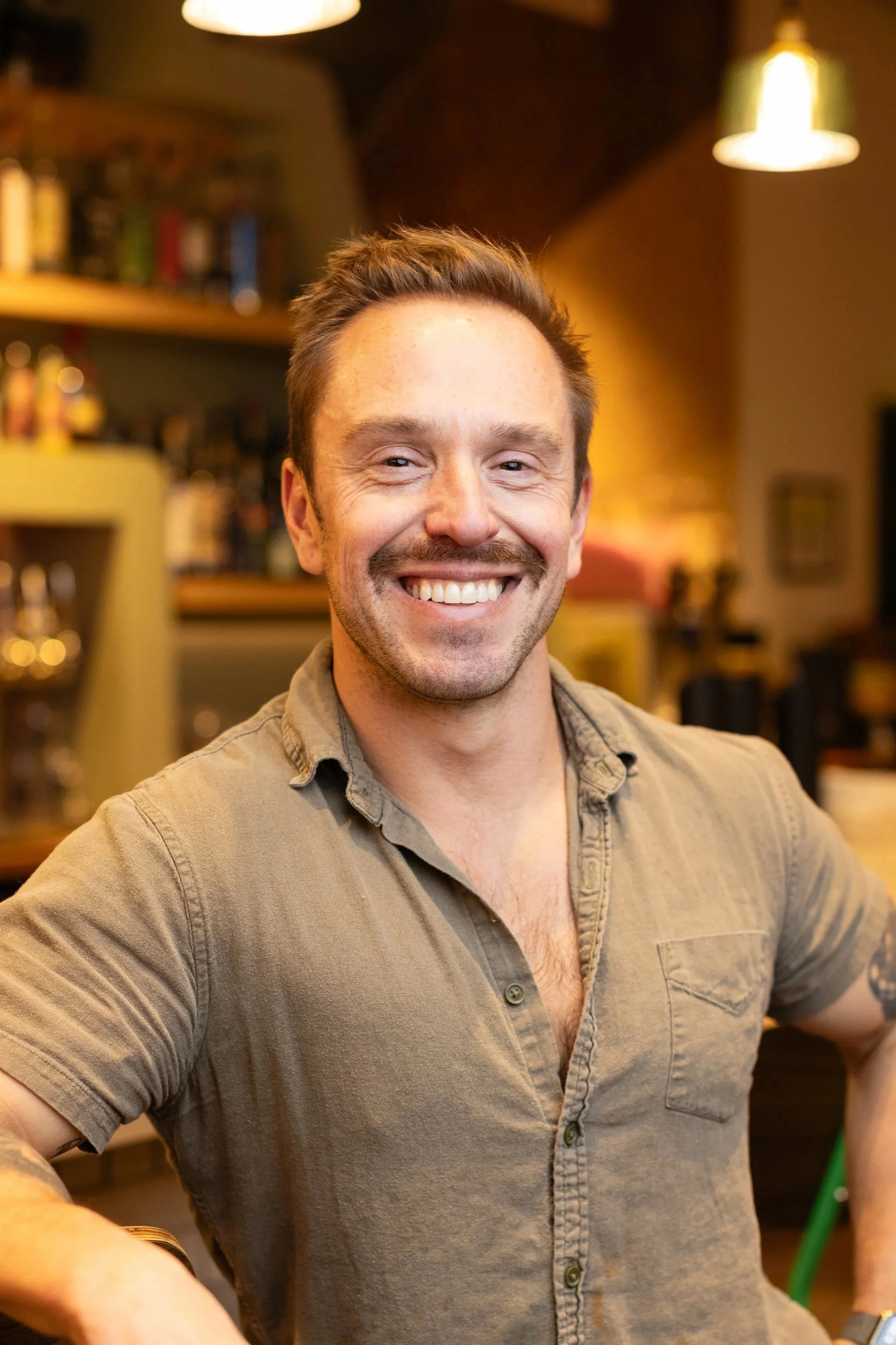 A man holding a glass of beer inside a restaurant or bar with a sign that reads 'Maiz' in the background.