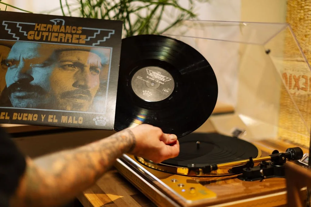 Person placing a black vinyl record on a turntable with a cover showing a portrait of Hermando Gutierrez and the text "Hermando Gutierrez El Bueno Y El Malo".