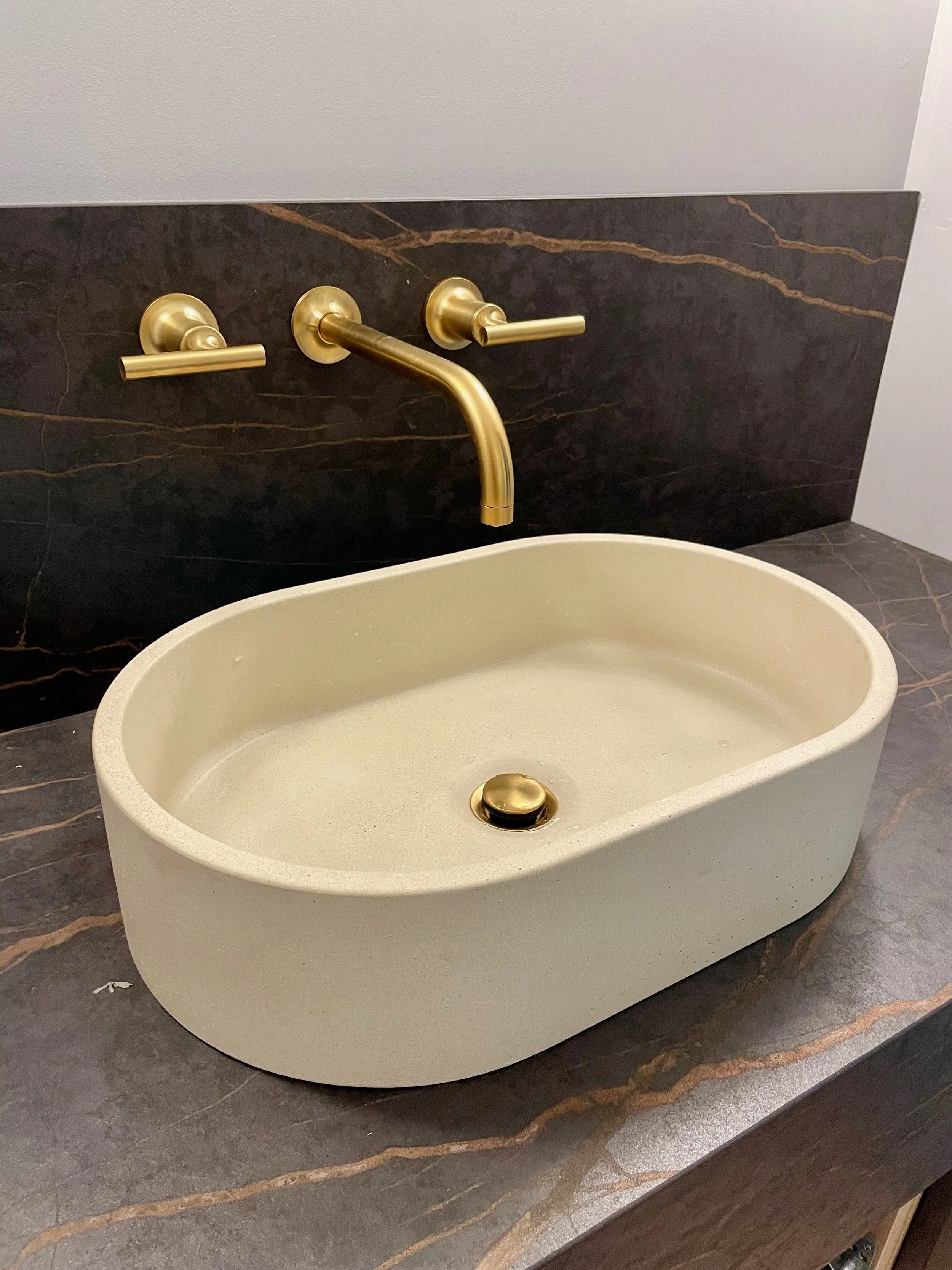 Modern bathroom sink with gold fixtures and black marble backsplash. Installed by Bluestone Plumbing.