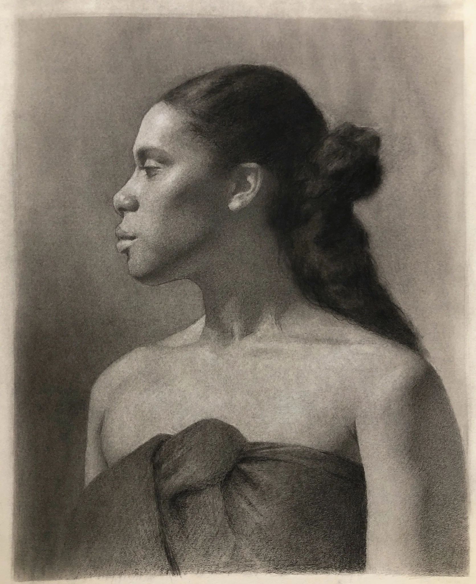 A black and white portrait of a woman with dark hair tied back, shown in profile, wearing a strapless top with a bow detail.