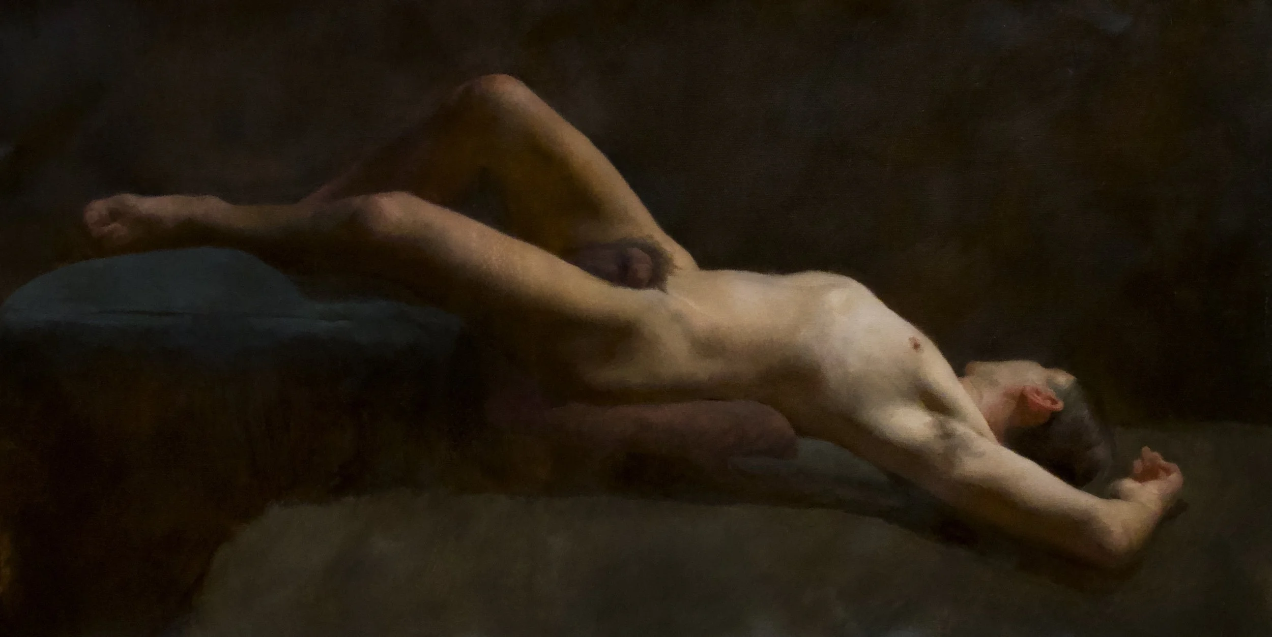 A nude man lying on his back on a dark surface with arms extended overhead and legs bent, resting their head on their arms in a relaxed pose.