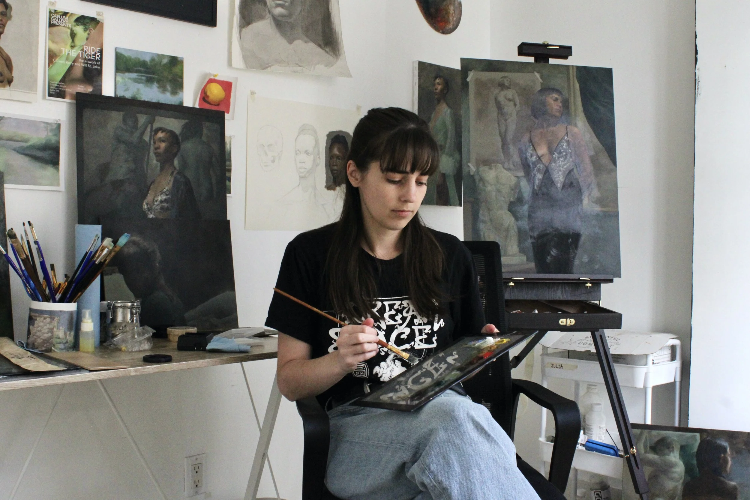 Young woman painting or drawing on a canvas in her art studio, surrounded by paintings, sketches, and art supplies.