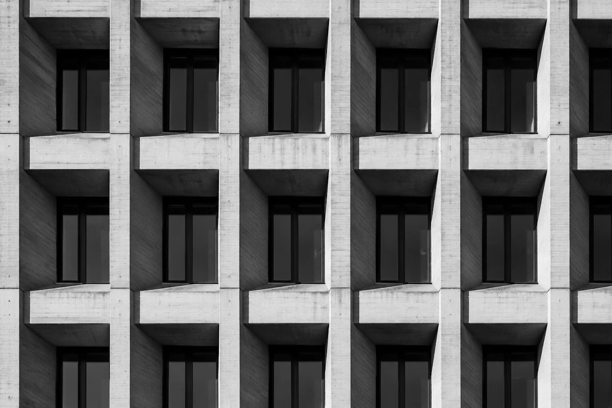 Repeating concrete window grid in sharp light — organisational legibility as the real AI moat