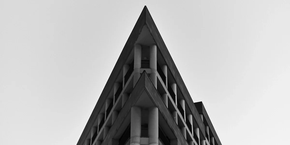A black and white photo of a modern building with a triangular roof and multiple balconies, viewed from below.