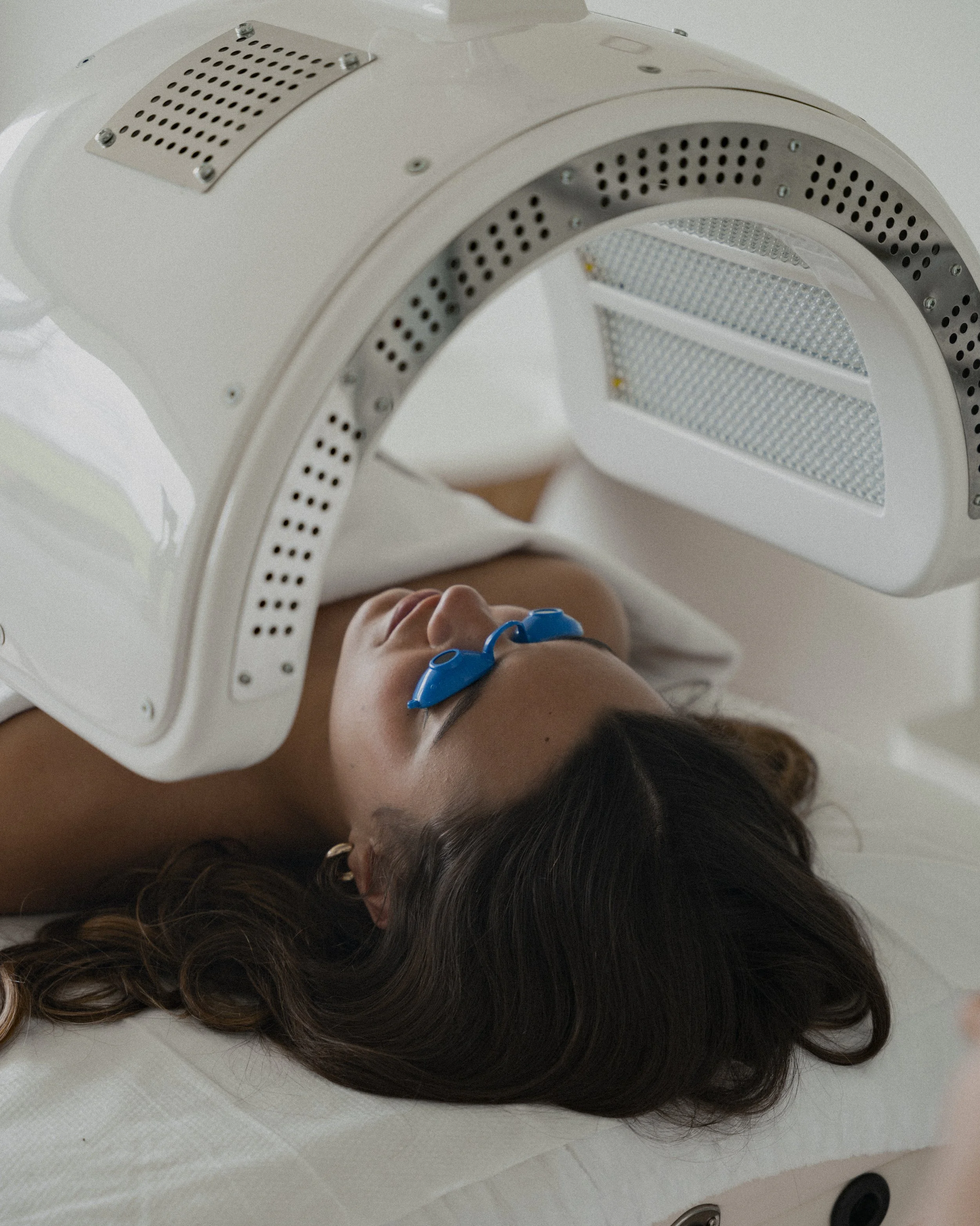 Vrouw ligt onder een medische apparaat dat een scan uitvoert, ze draagt brillen en ligt op een bed.