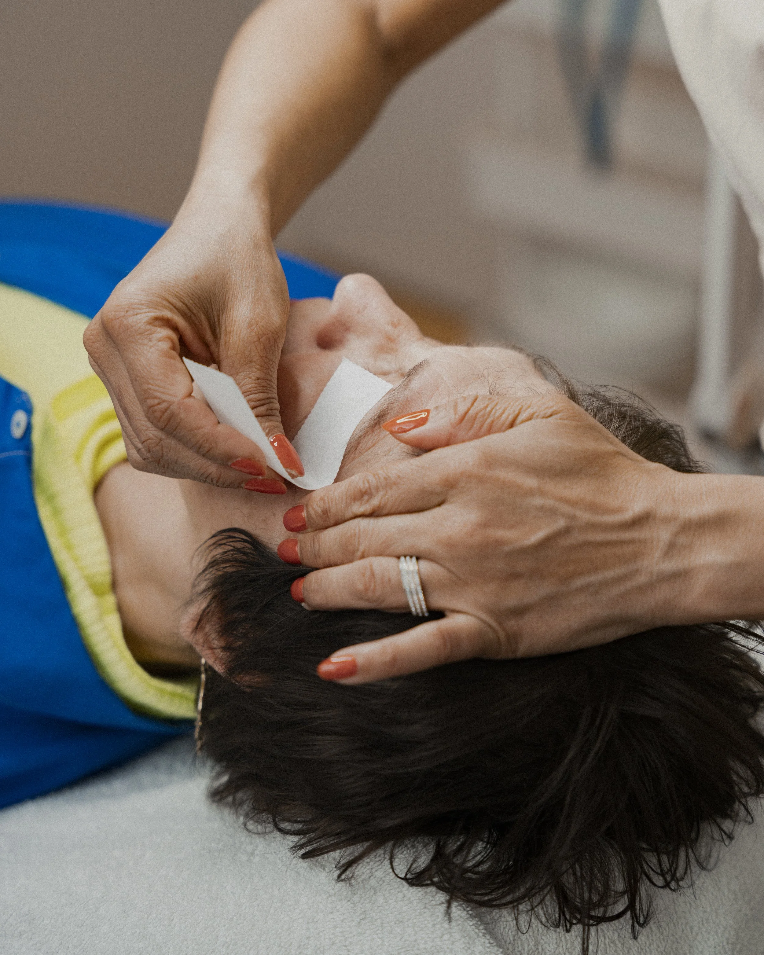Persoon krijgt hulp bij het schoonmaken of verzorgen van het gezicht, liggend op een bed of tafel.
