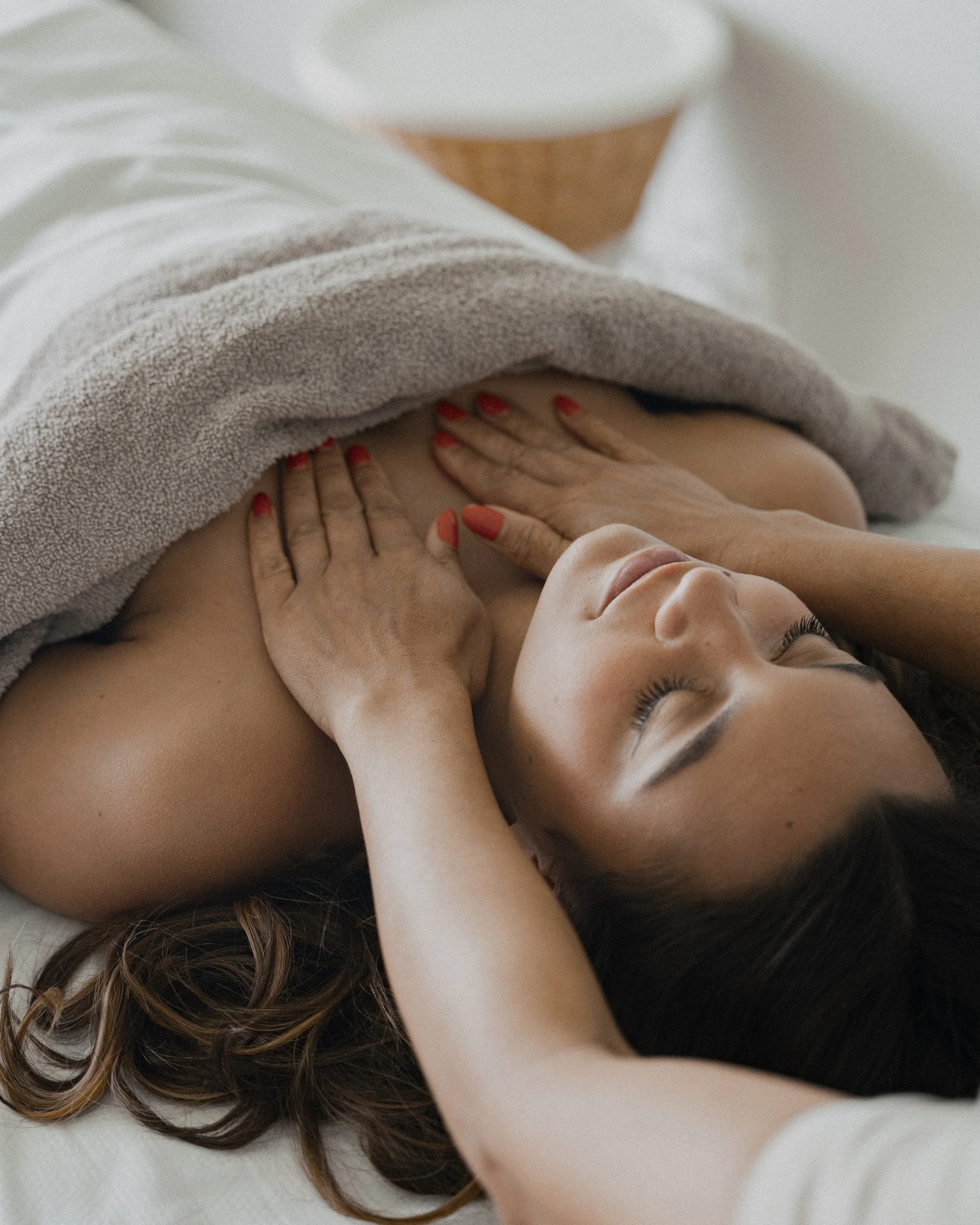 Vrouw ligt ontspannen op haar rug met handen op haar borst, onder een beige badjas, in een rustige omgeving.