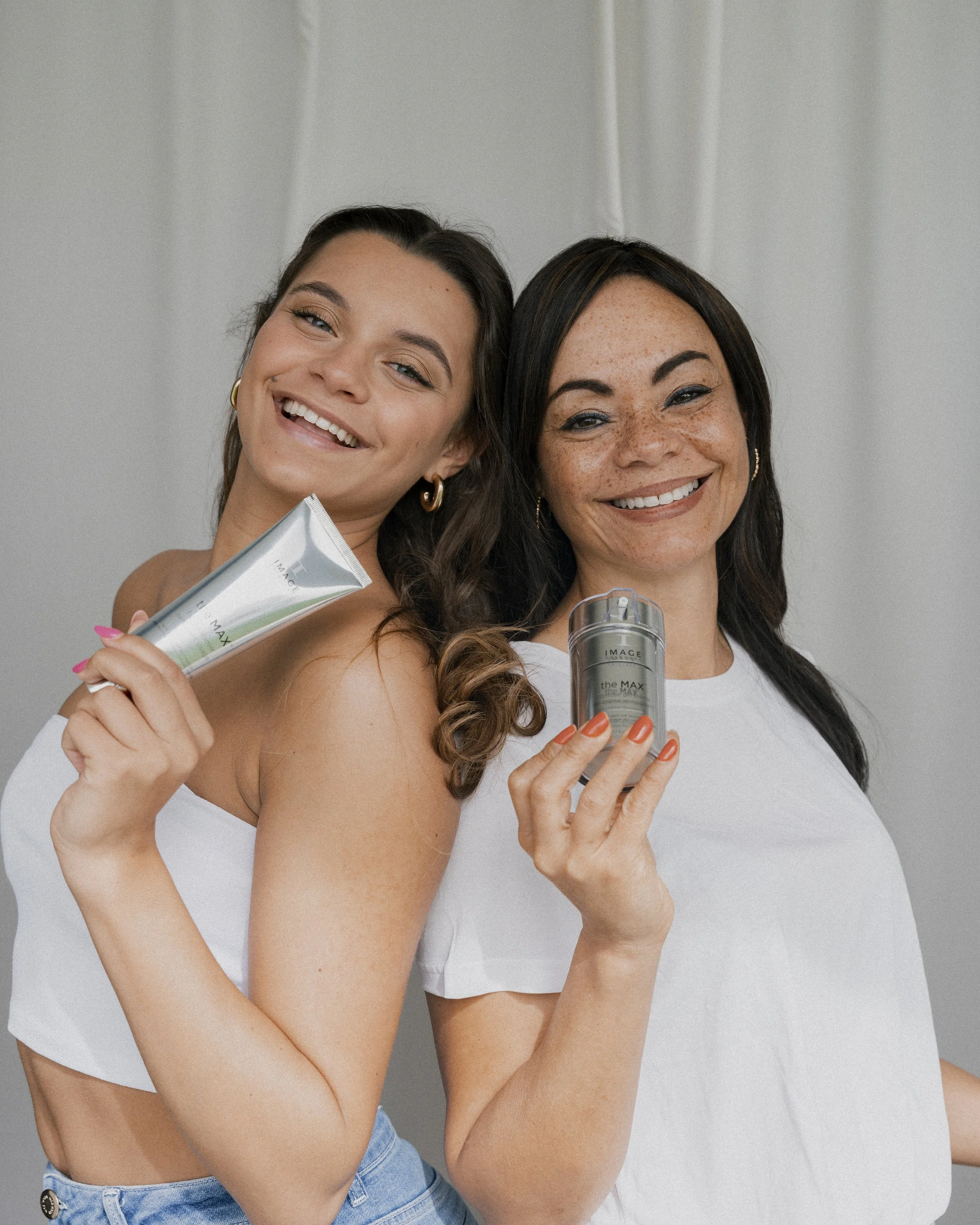 Twee vrouwen lachen en houden skincareproducten vast.