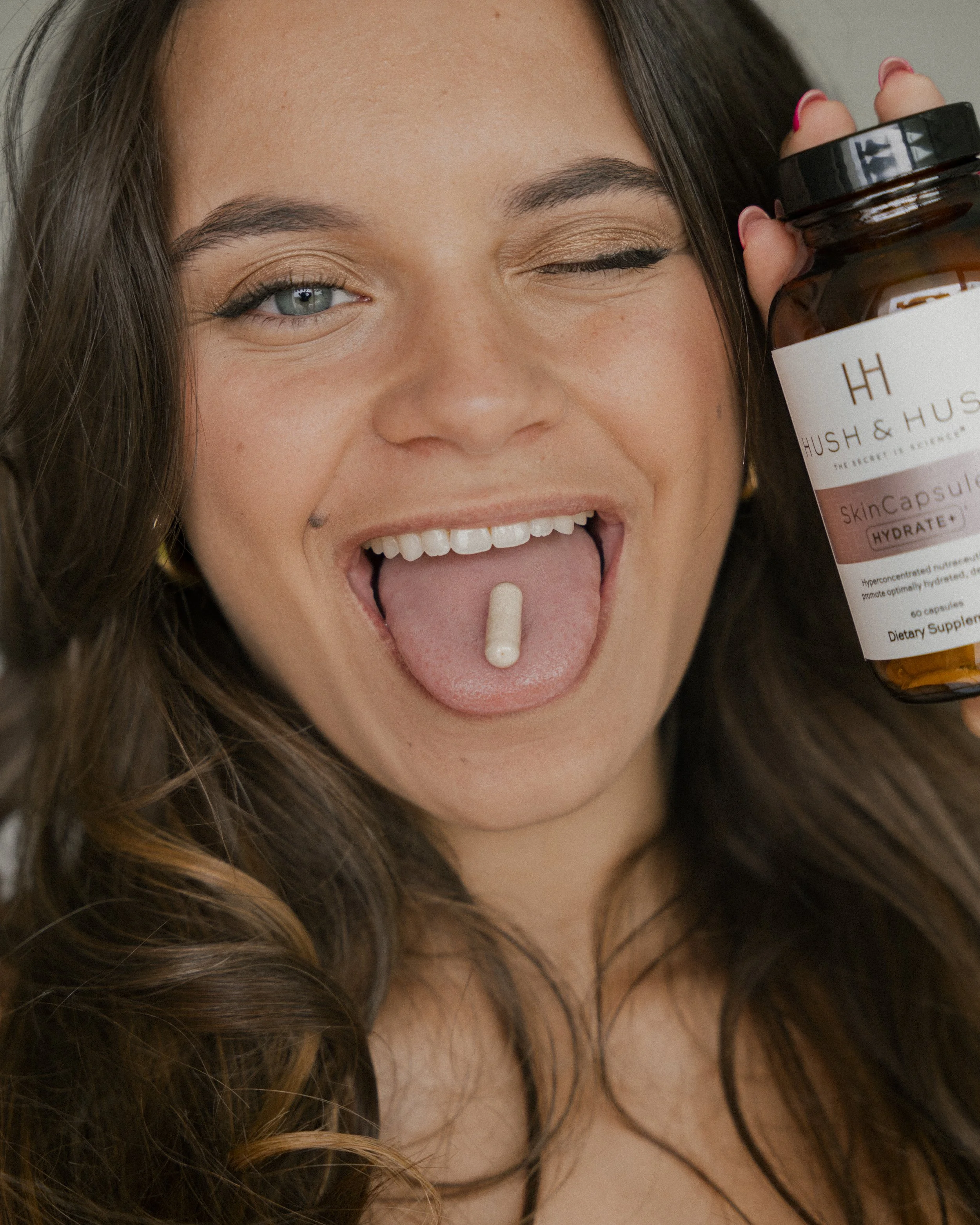 Vrouw met lang bruin haar houdt een fles supplementen en toont een capsule op haar tong.