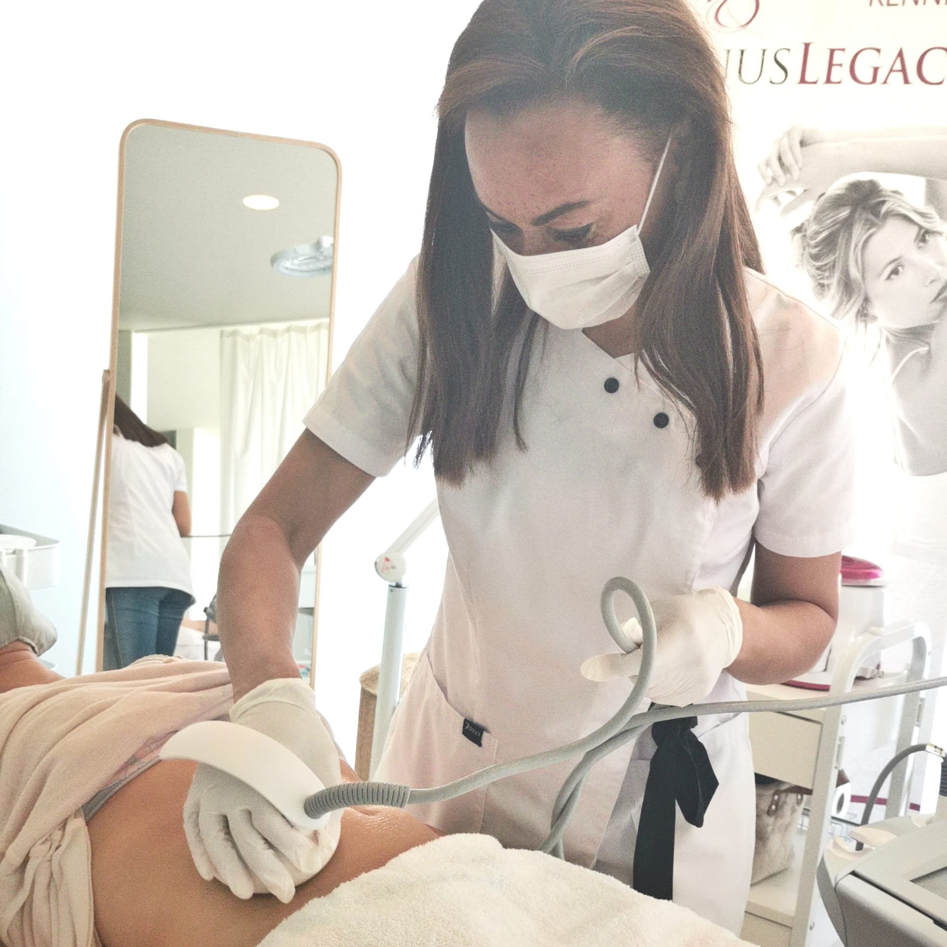 Een verpleegkundige voert een medische procedure uit op een patiënt in een kliniek, beide dragen maskers en handschoenen.