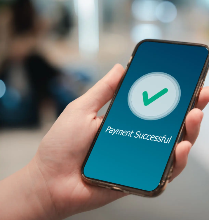 Hand holding a smartphone displaying a confirmation screen with a green checkmark and the text 'Payment Successful'.