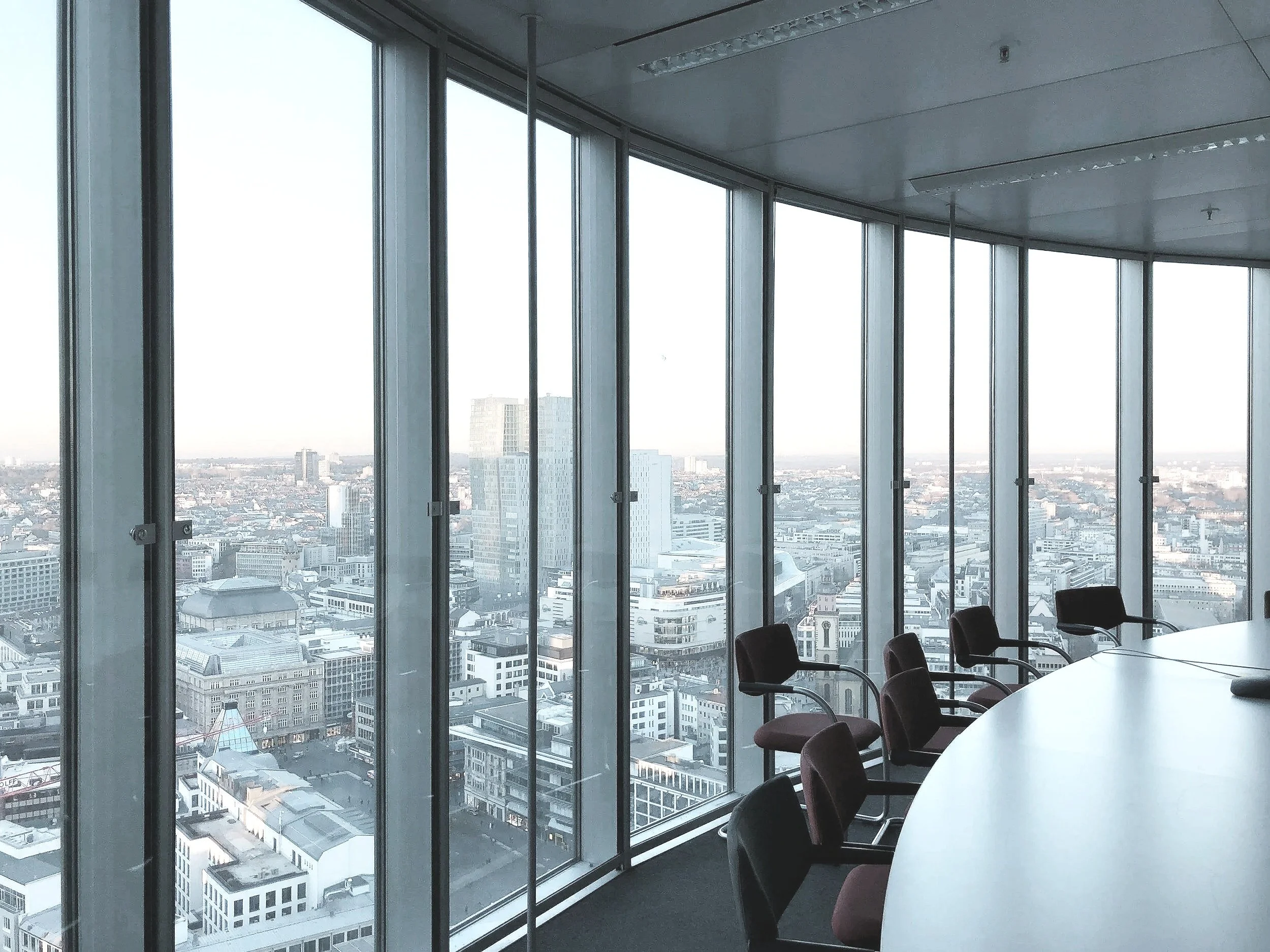 Modern conference room located in the GTA, with floor-to-ceiling windows overlooking a city skyline, round table, and office chairs.