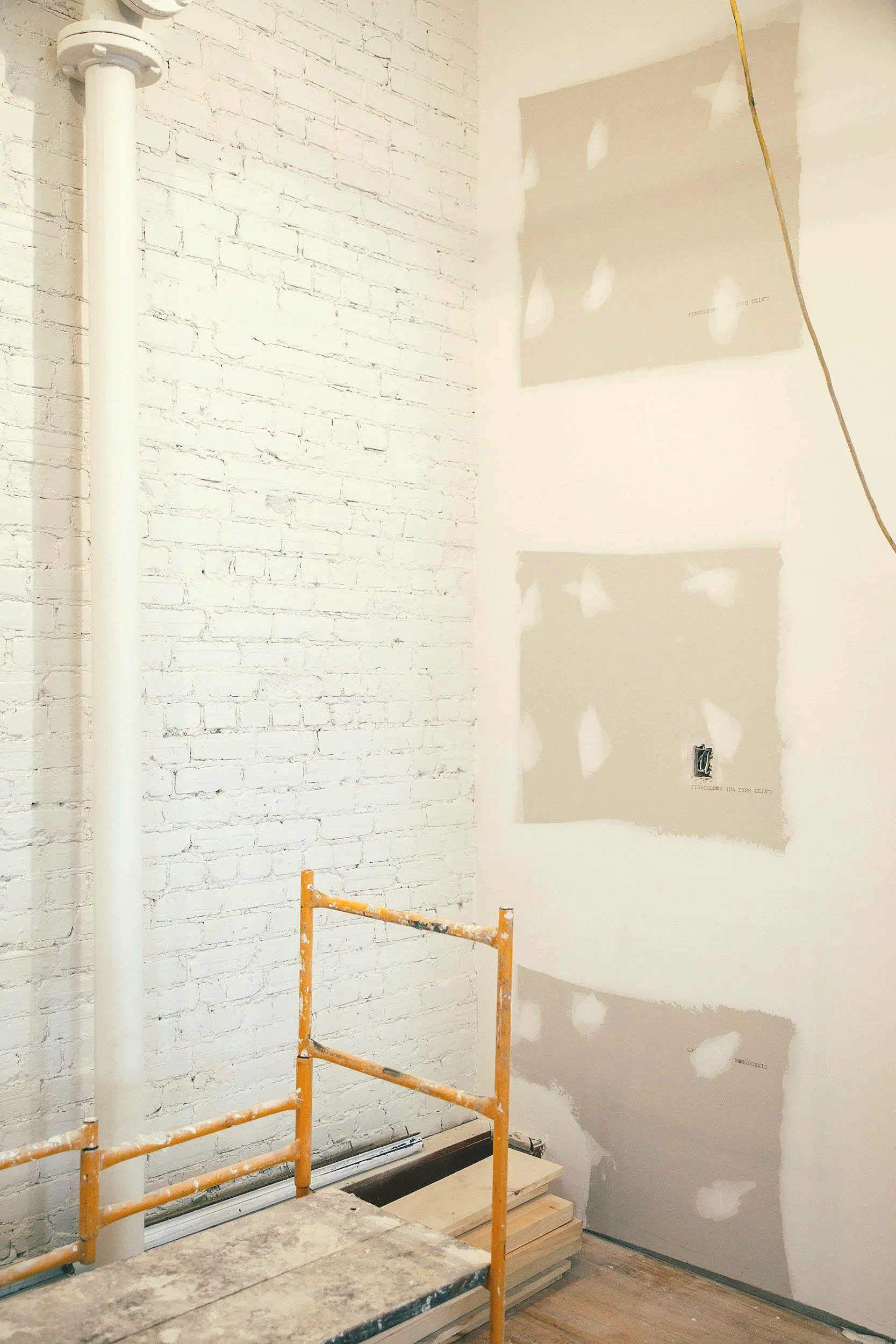 Interior space under renovation in the GTA Toronto with a white-painted brick wall, unfinished drywall, an orange scaffolding, and construction materials on the floor.
