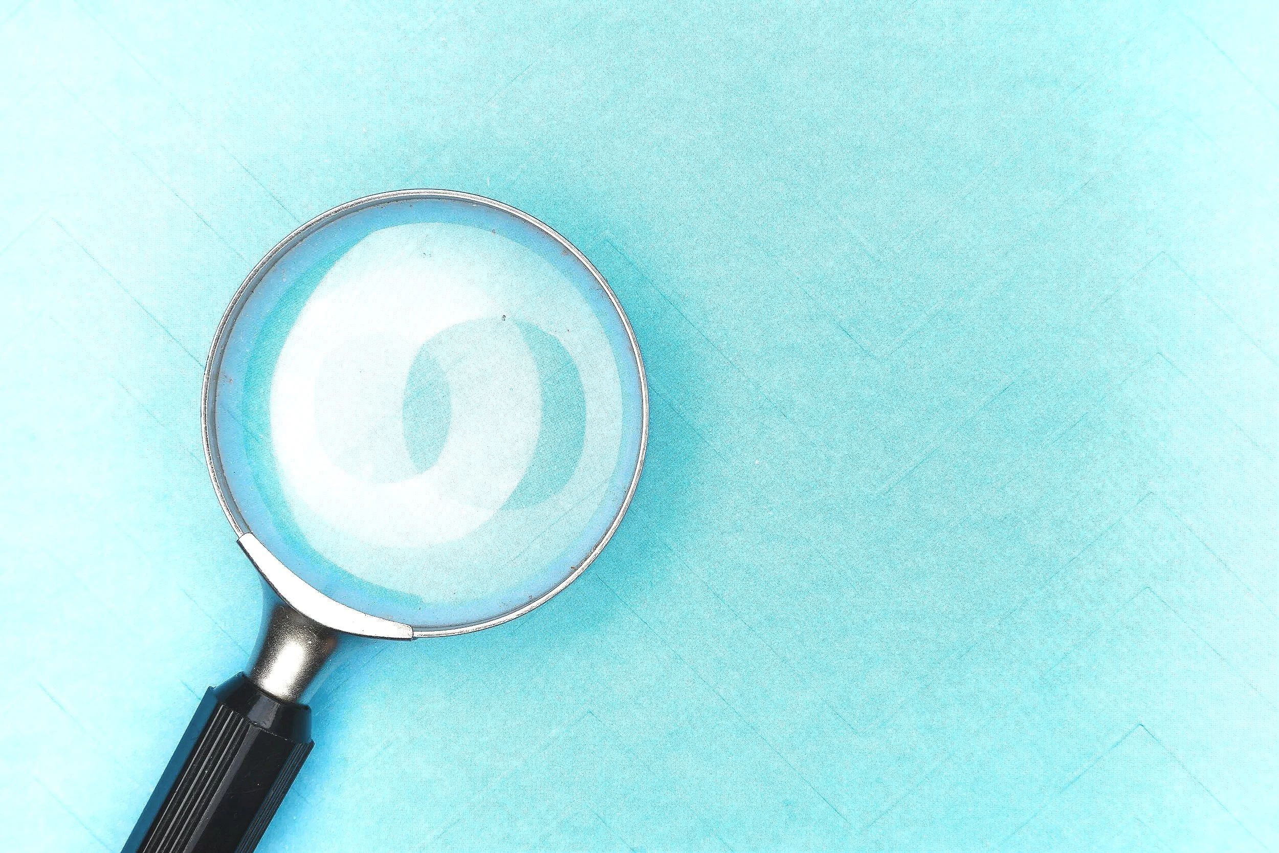 A magnifying glass with a black handle placed on a light blue surface.