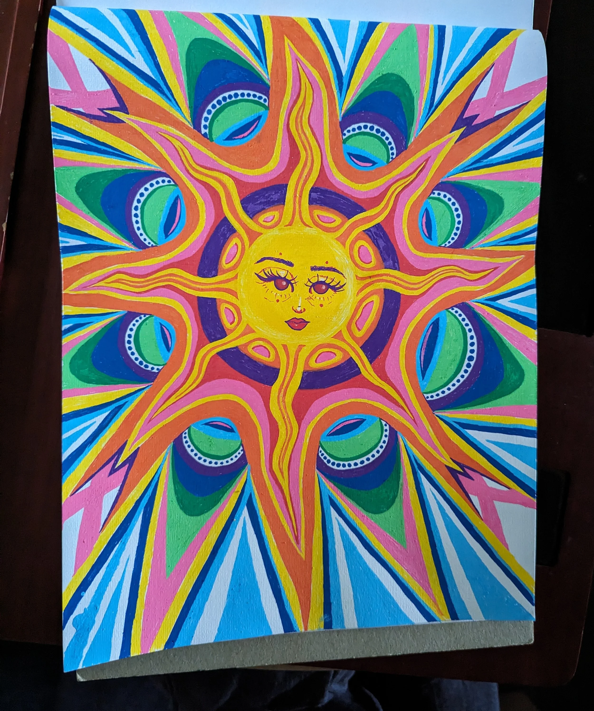Colorful abstract artwork of a sun with a woman's face, vibrant pink, yellow, blue, green, and purple colors, stylized with patterns and details.